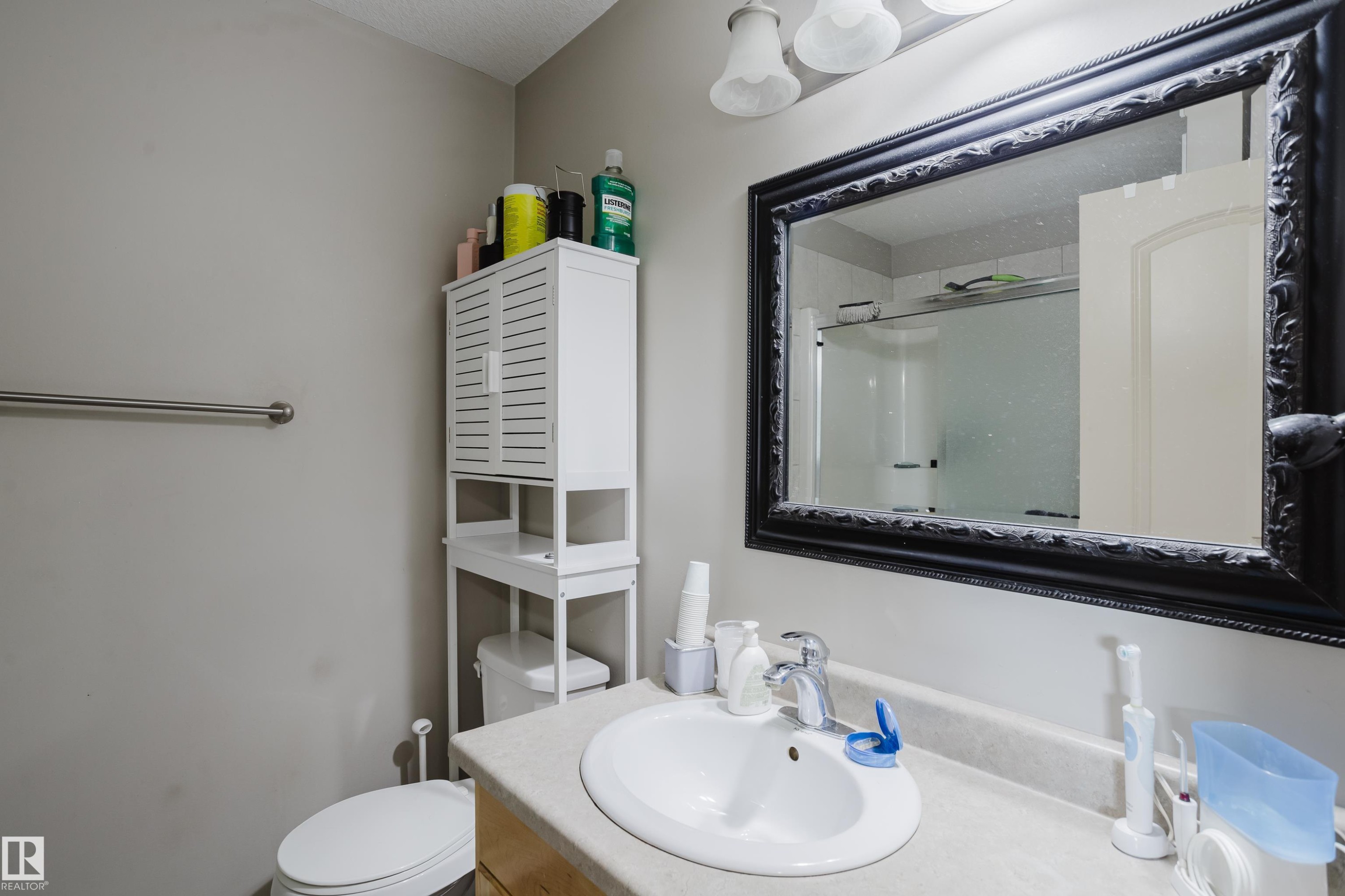 Bathroom featuring a vanity with an integrated sink, a large framed mirror, and a white over-the-toilet storage cabinet - 10334 161 Street Nw, Edmonton, AB