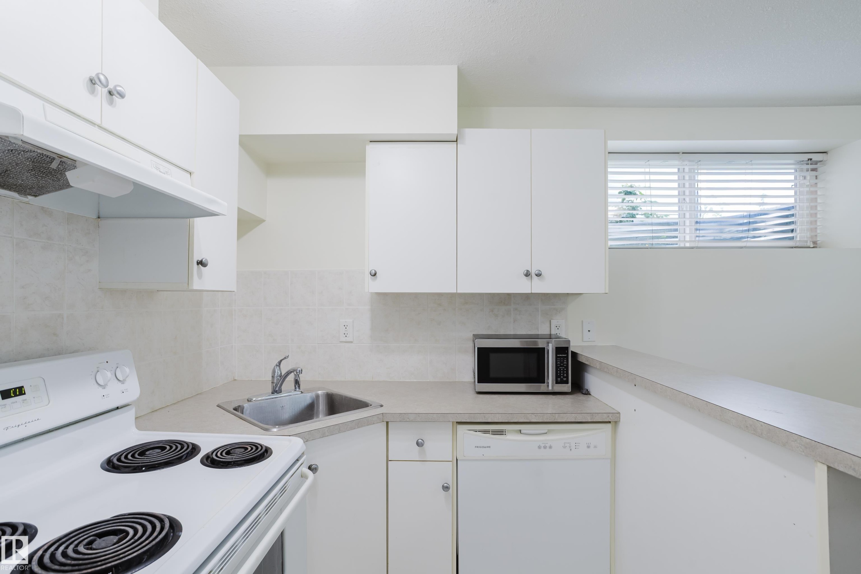 White cabinetry and countertop space with a stainless steel sink, tile backsplash, and built-in dishwasher - 10334 161 Street Nw, Edmonton, AB