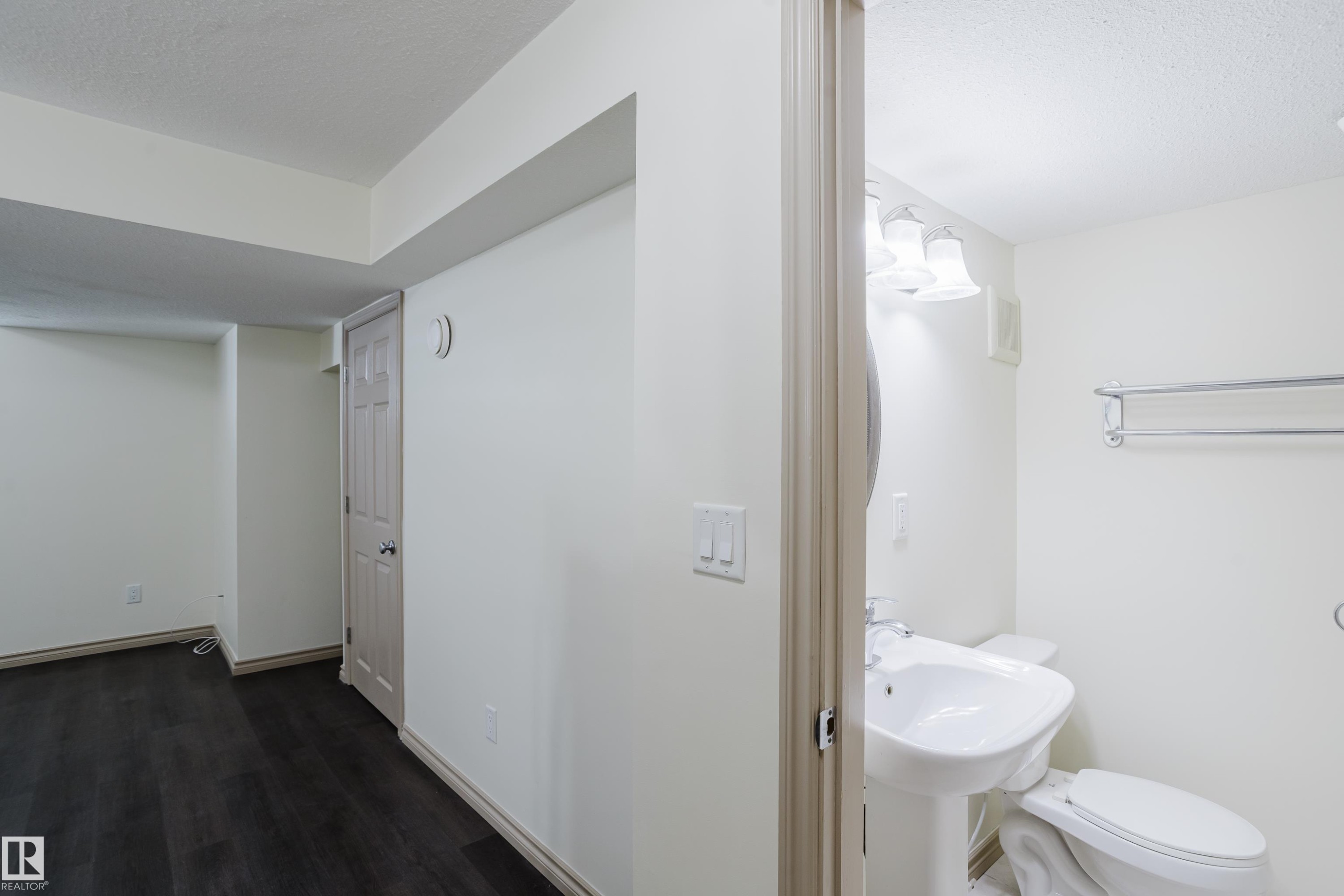 Pedestal sink, wall-mounted vanity lighting, and chrome towel bar in the bathroom - 10334 161 Street Nw, Edmonton, AB