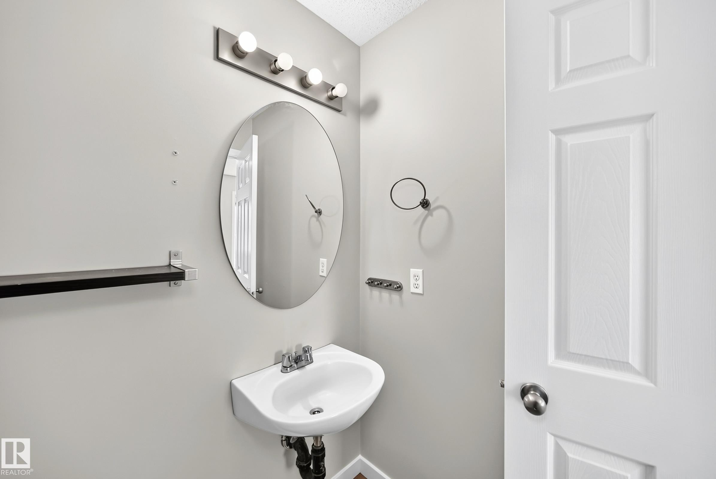 Wall-mounted sink with a chrome faucet, illuminated by a four-bulb vanity light fixture - 203 84 Street Sw, Edmonton, AB - Indoor Photo Showing Bathroom