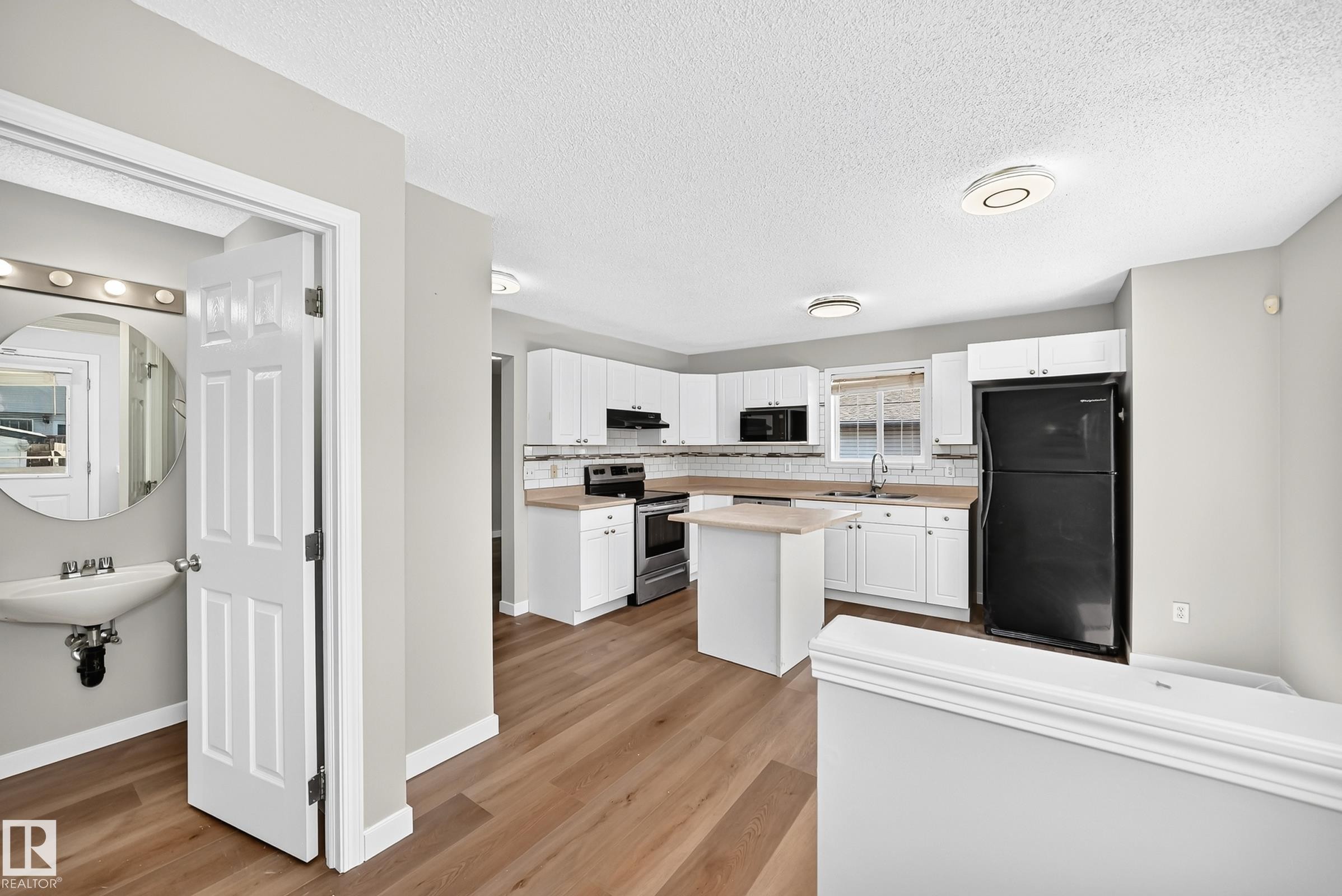 Open-concept kitchen featuring white cabinetry, light countertops, subway tile backsplash, and wood-finish flooring - 203 84 Street Sw, Edmonton, AB - Indoor Photo Showing Kitchen