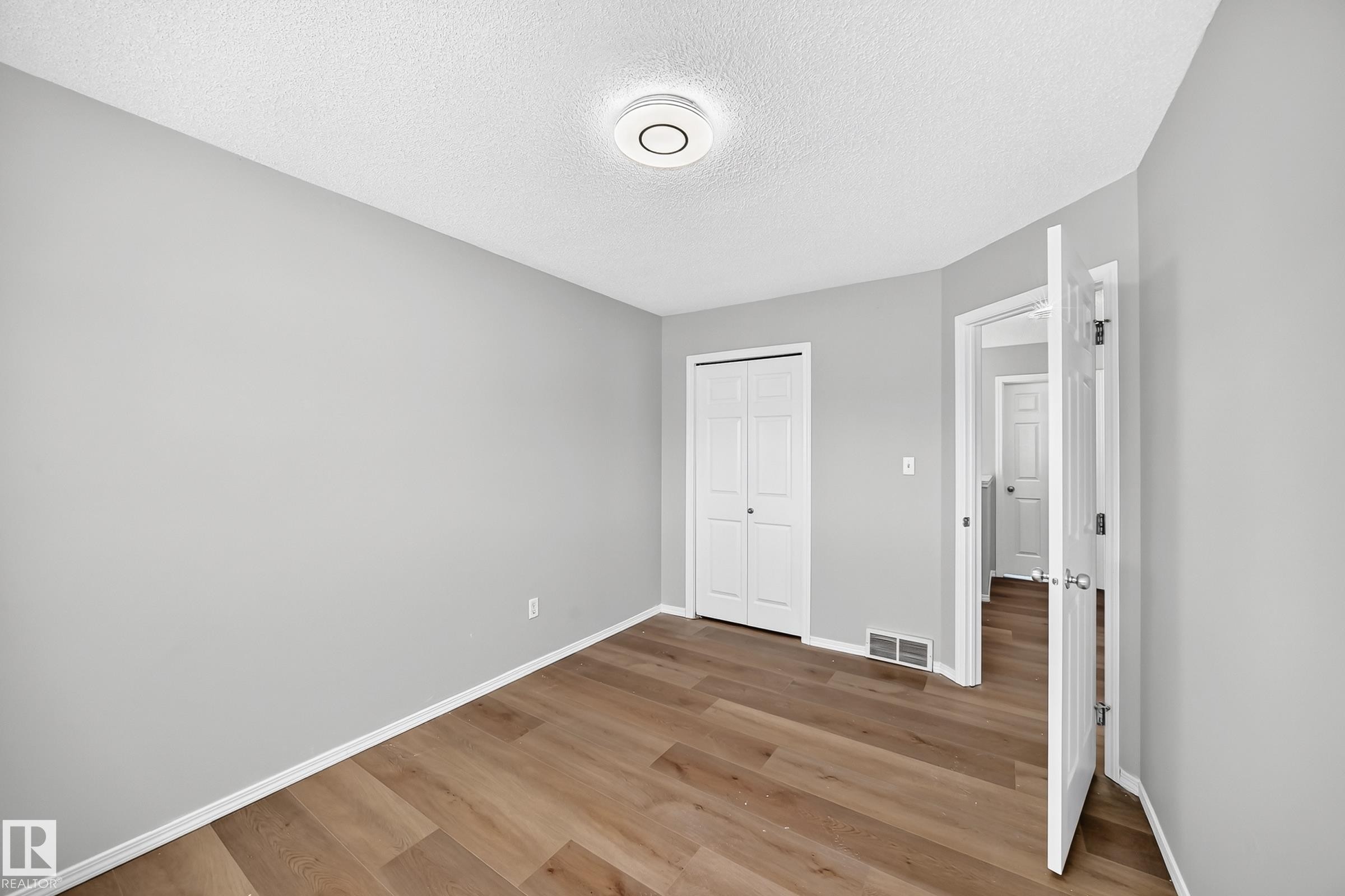 Room featuring wood-finish flooring, light gray walls, white baseboards, and a ceiling-mounted light fixture - 203 84 Street Sw, Edmonton, AB - Indoor Photo Showing Other Room