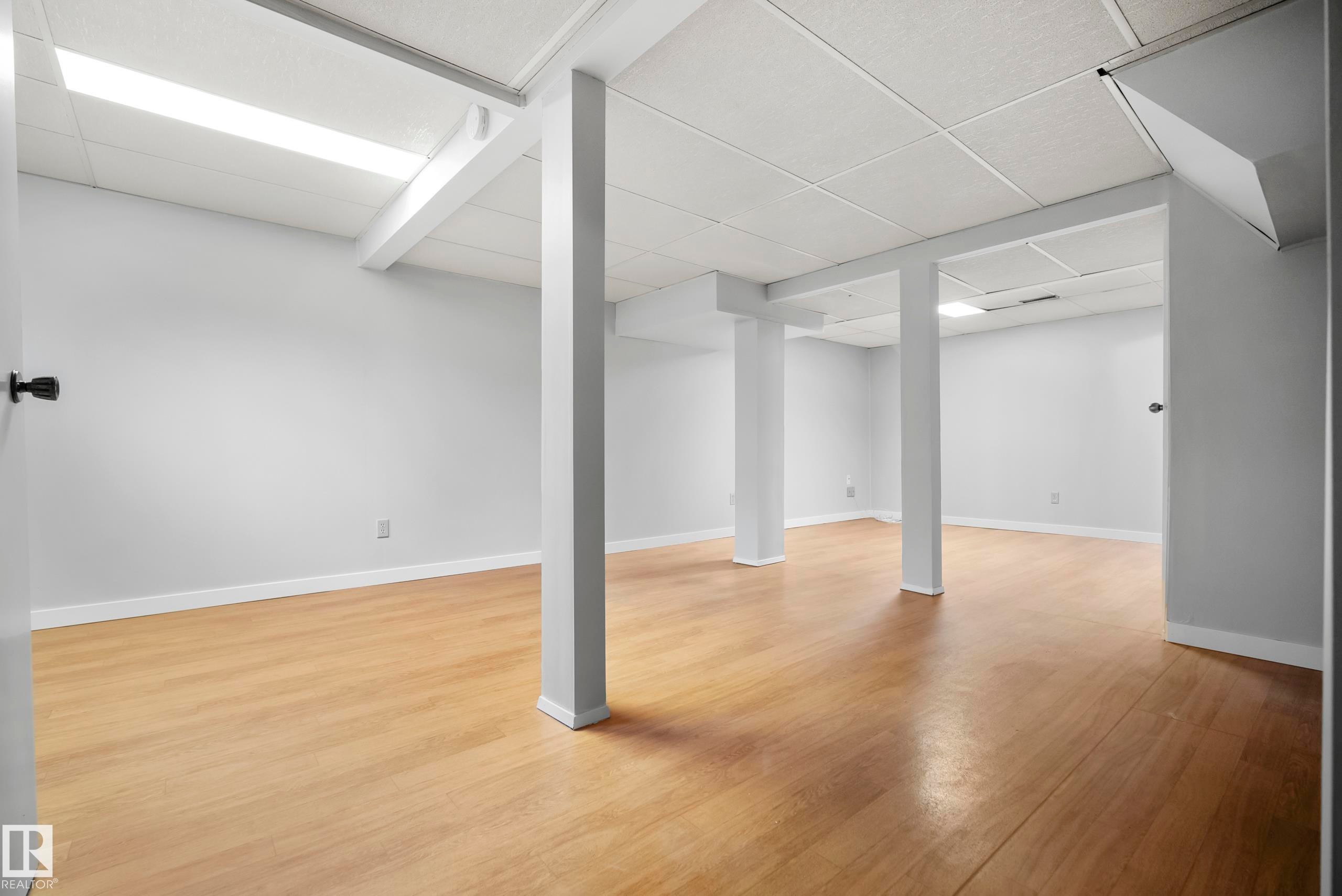 Expansive room featuring wood-finish flooring, drop ceiling with integrated lighting, and neutral wall paint - 3173 139 Avenue Nw, Edmonton, AB