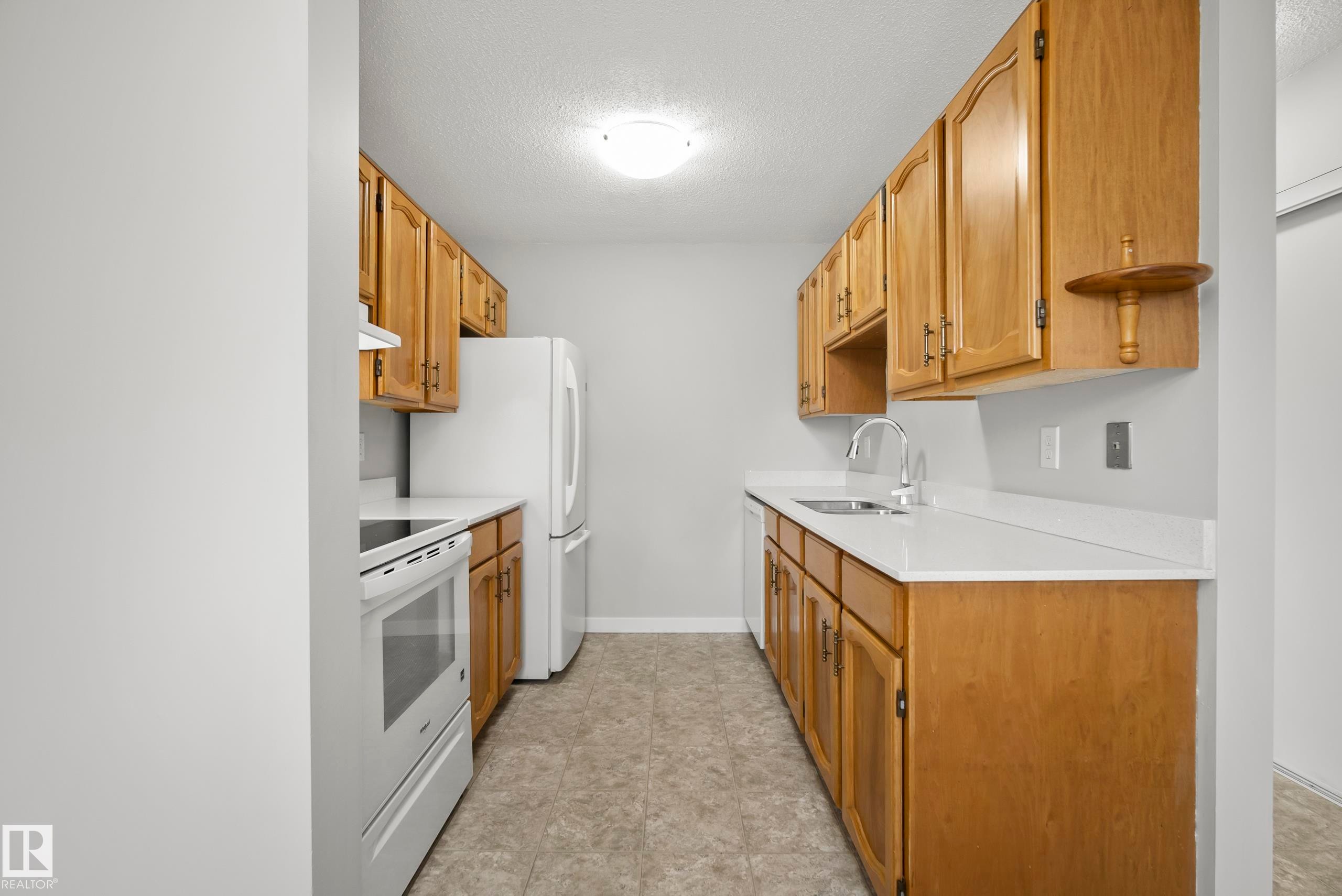 Galley kitchen featuring wood-finish cabinetry, white countertops, a stainless steel sink with a chrome faucet, and a white electric range - 3173 139 Avenue Nw, Edmonton, AB