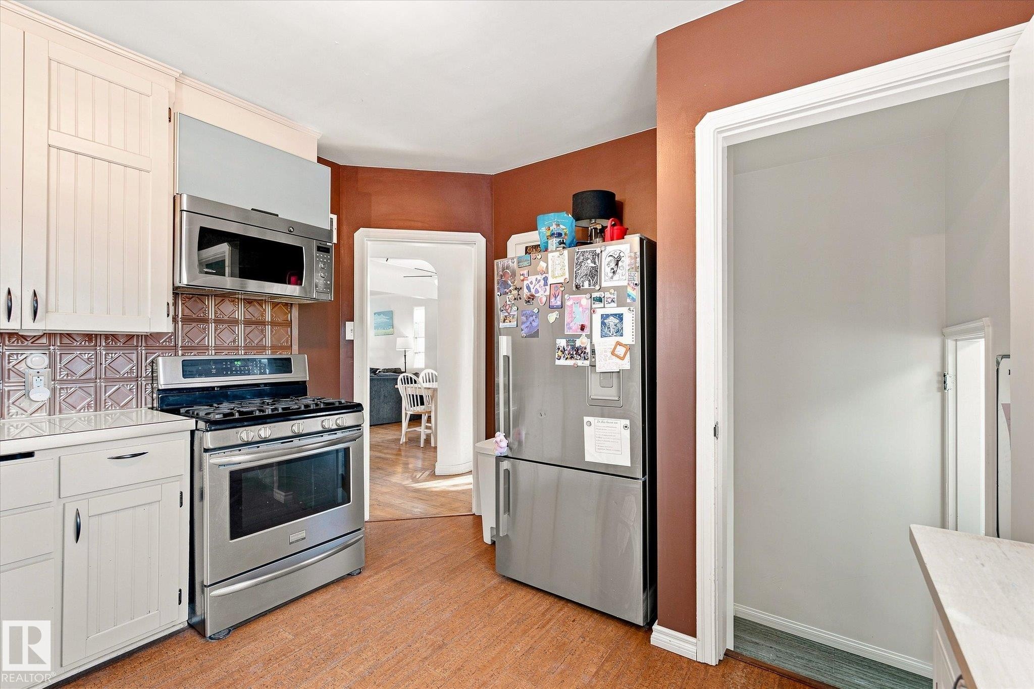 White cabinetry, stainless steel appliances, patterned backsplash, wood-finish flooring, and a pantry with shelving - 10943 72 Avenue Nw, Edmonton, AB