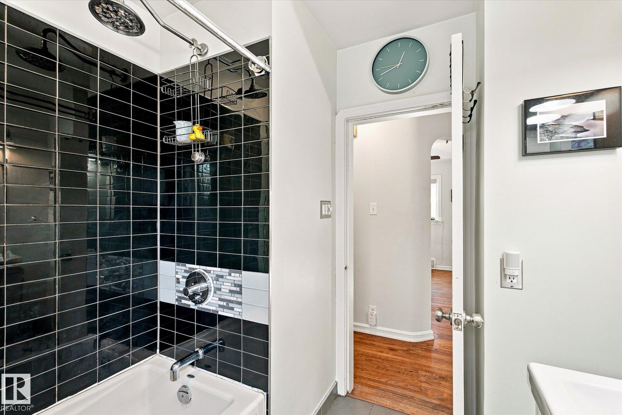 Bathtub with a black subway tile surround, mosaic accent tile, and a dual shower head system - 10943 72 Avenue Nw, Edmonton, AB