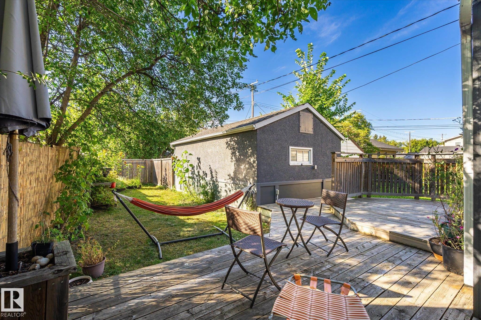 Expansive backyard featuring a wood deck, manicured lawn, and mature trees - 10943 72 Avenue Nw, Edmonton, AB