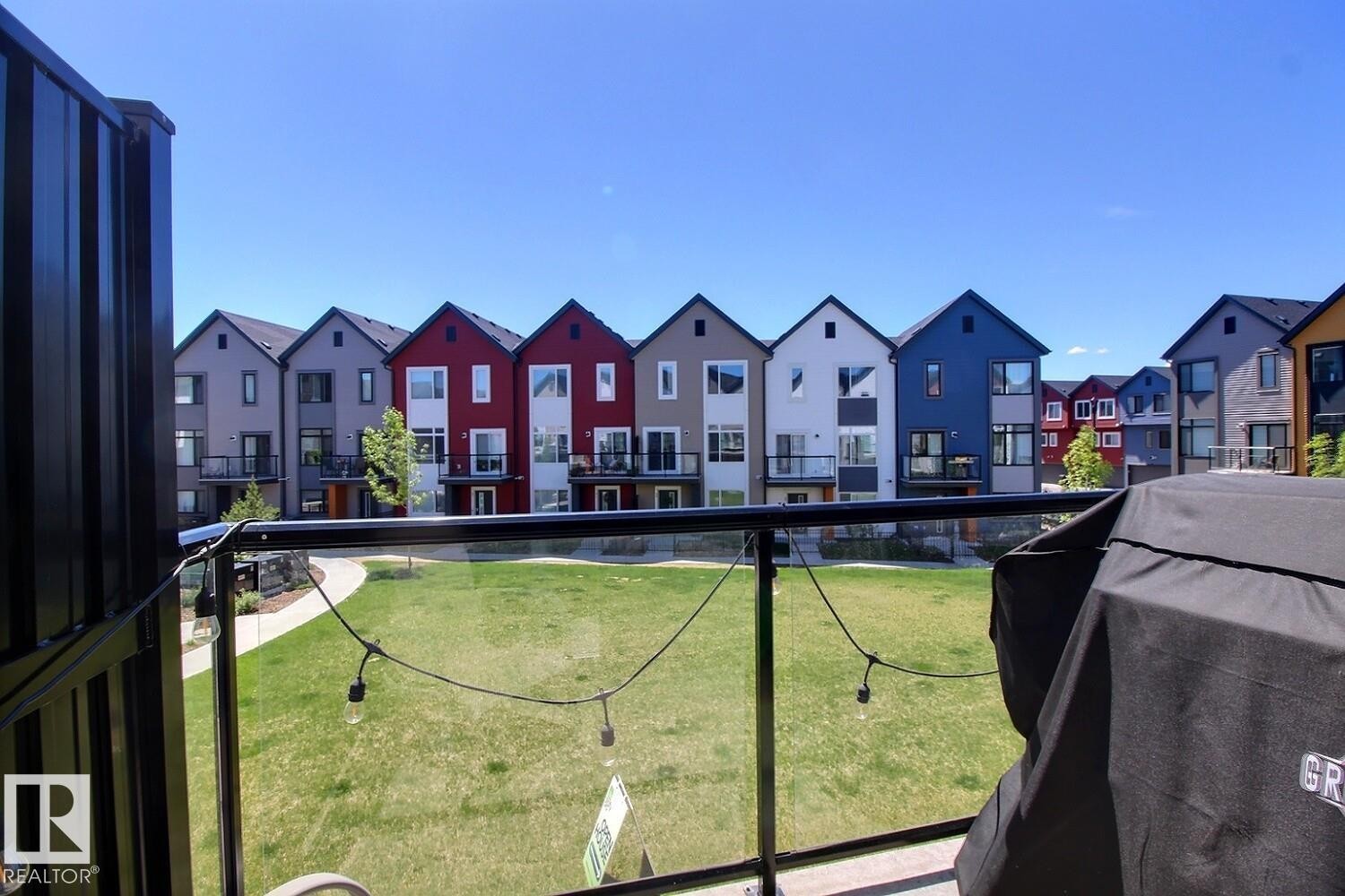 Balcony with glass railing overlooking a communal green space with a paved pathway - #99 1010 Rabbit Hill Rd Sw, Edmonton, AB