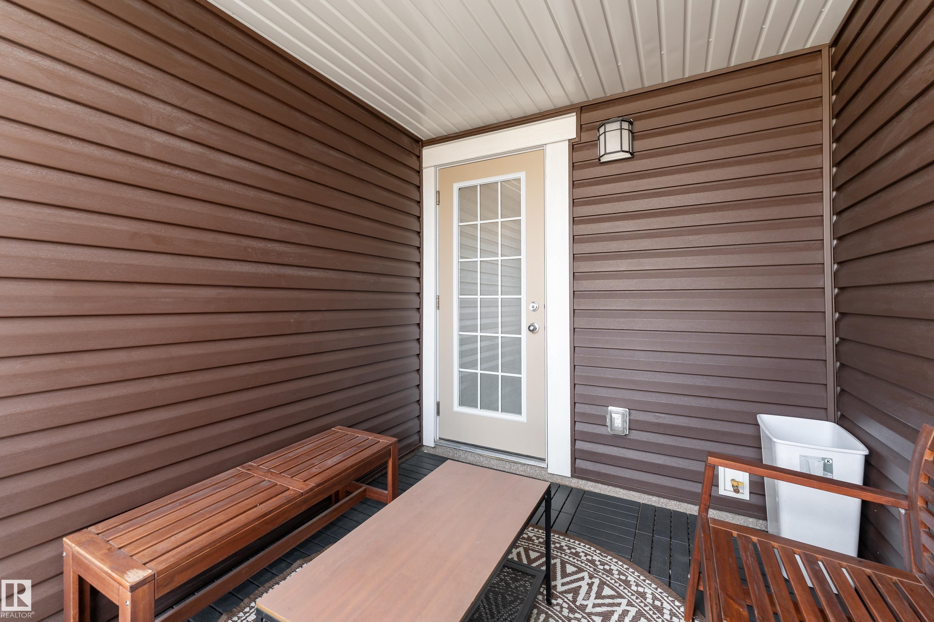 Outdoor patio featuring dark wood-finish siding, a white privacy door, an overhead light fixture, and a slatted ceiling - 20247 16 Avenue Nw, Edmonton, AB