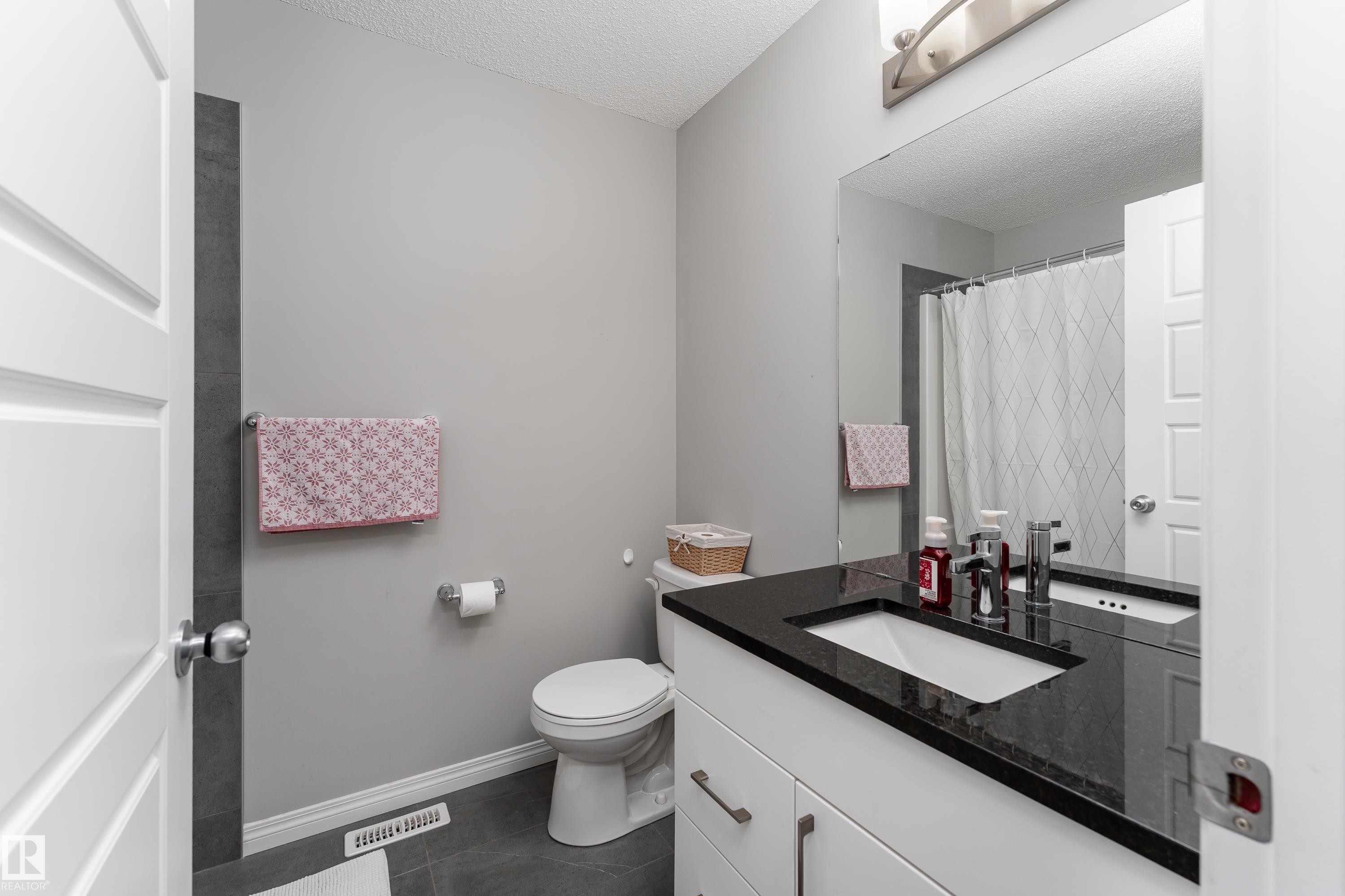 White vanity with dark countertop, undermount sink, and brushed nickel hardware - 20247 16 Avenue Nw, Edmonton, AB