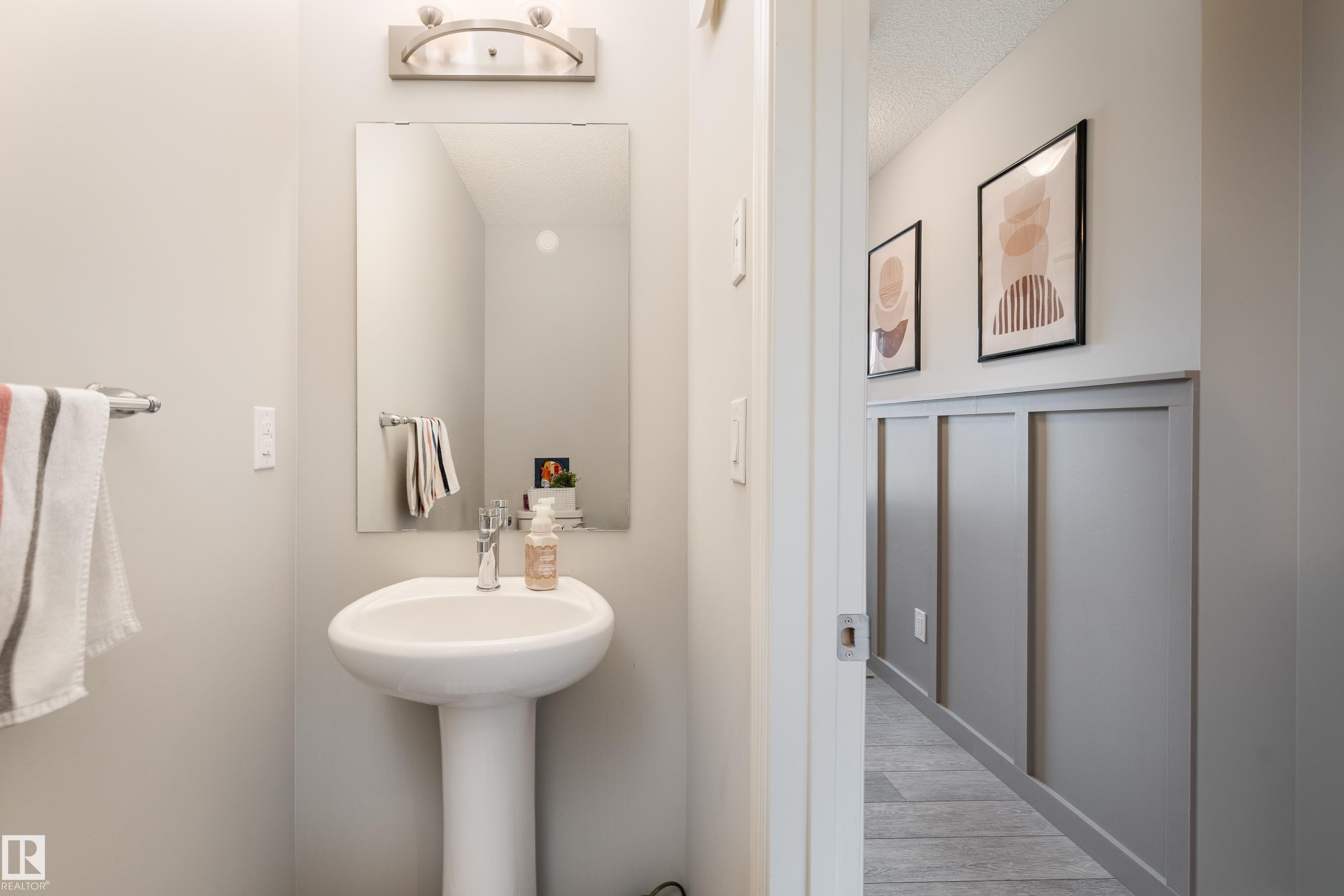 Pedestal sink with chrome faucet, rectangular mirror, and a wall-mounted light fixture - 20247 16 Avenue Nw, Edmonton, AB