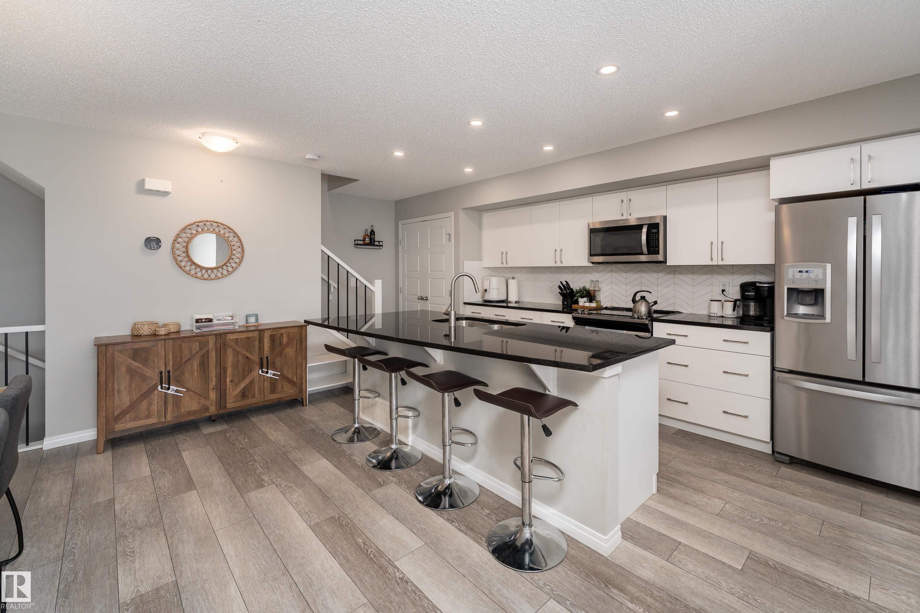 Well-appointed kitchen featuring wood-finish flooring, white cabinetry, a black island countertop, stainless steel appliances, and recessed lighting - 20247 16 Avenue Nw, Edmonton, AB