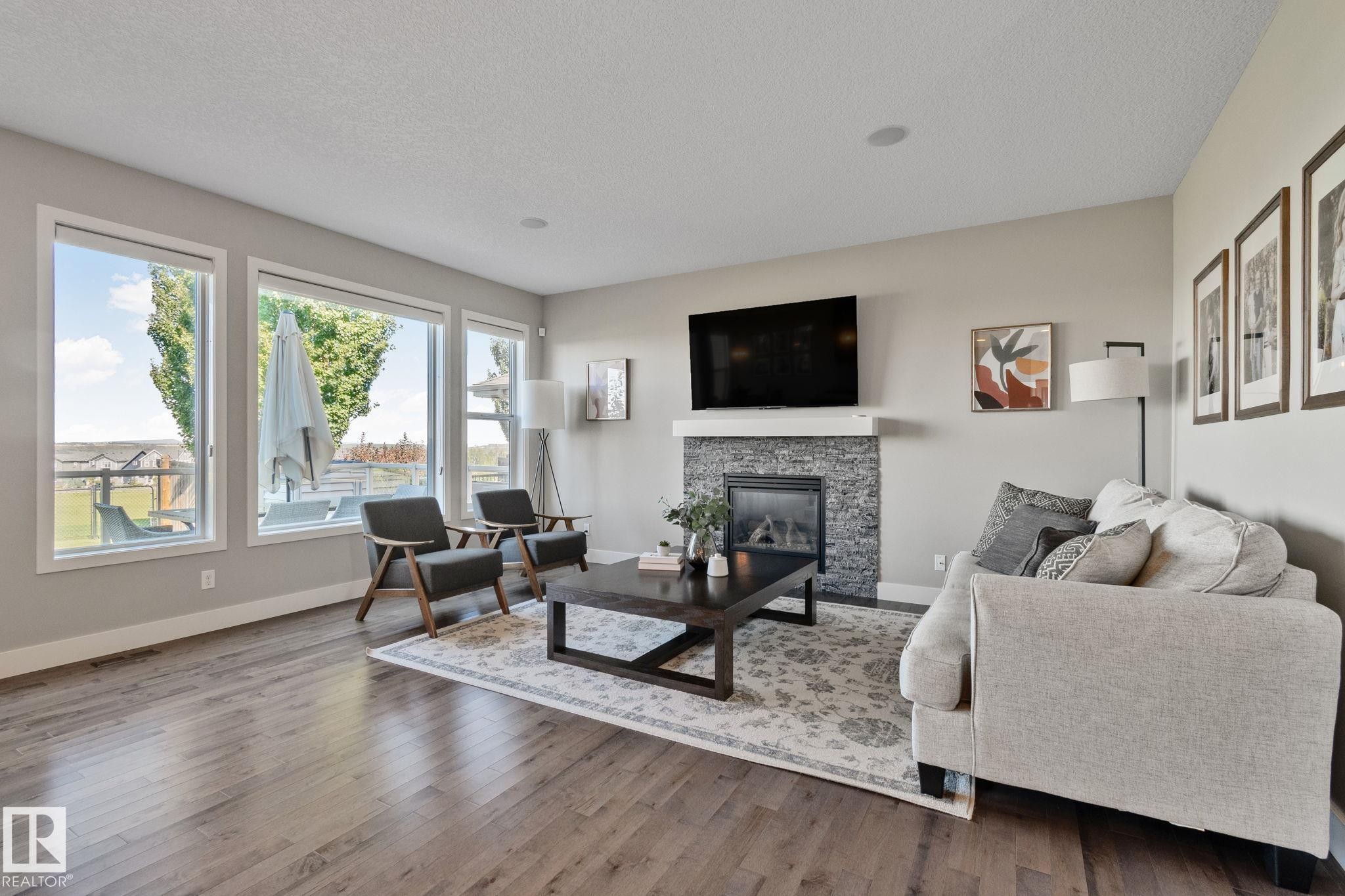 Wood-finish flooring throughout, a stone-clad fireplace with a white mantel, numerous windows, and recessed lighting - 2096 Redtail Common Nw, Edmonton, AB