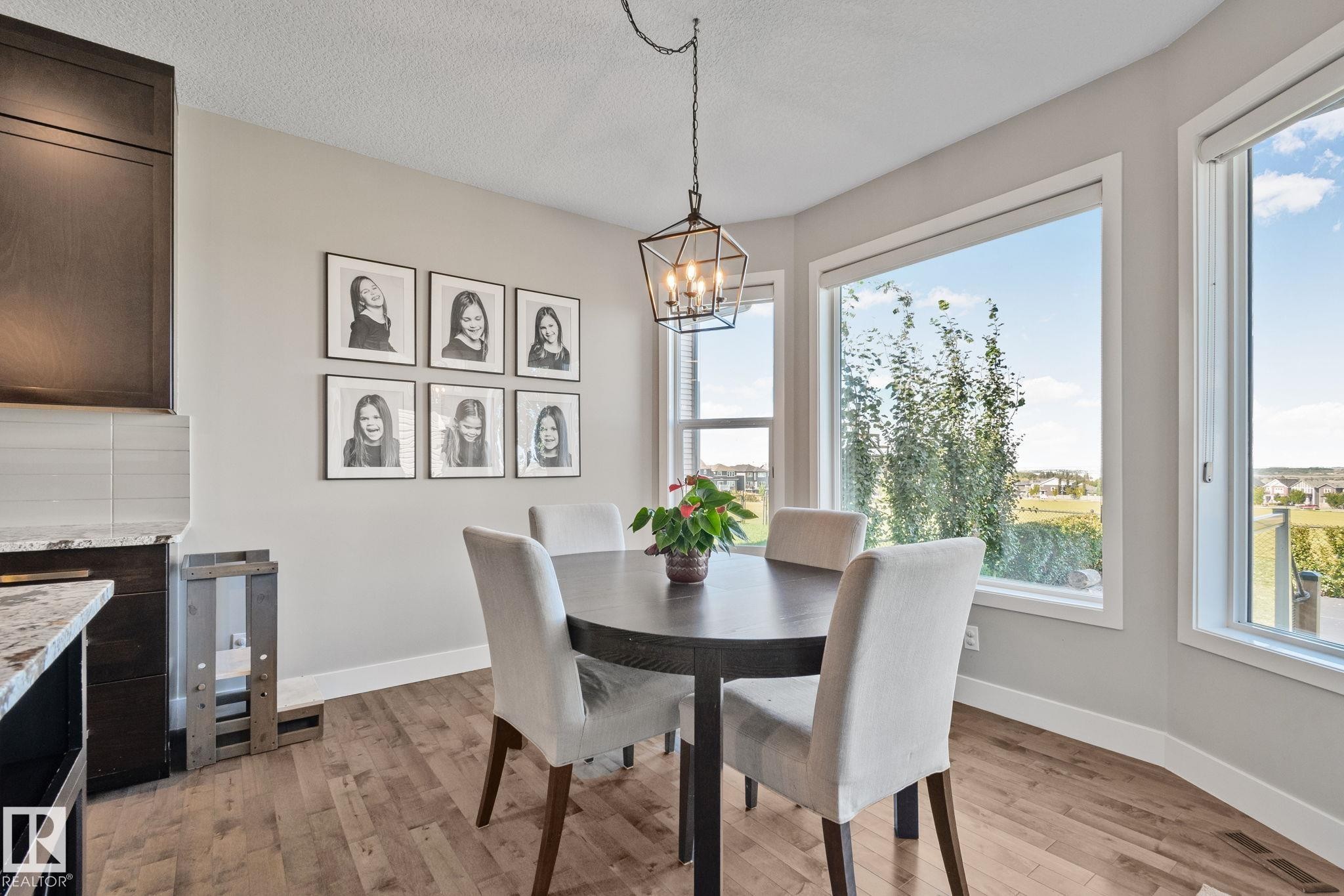 Bright dining area showcasing a round black table, upholstered dining chairs, and a pendant light fixture suspended from the ceiling - 2096 Redtail Common Nw, Edmonton, AB