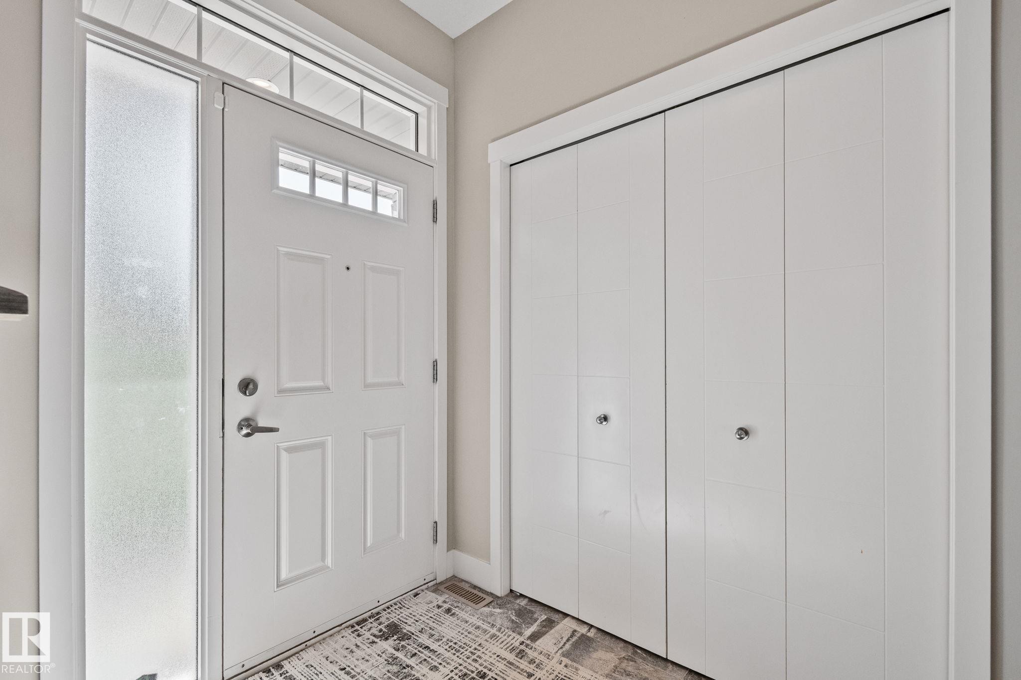 Entryway featuring a paneled door with transom window, frosted sidelight, and bi-fold closet doors - 2096 Redtail Common Nw, Edmonton, AB
