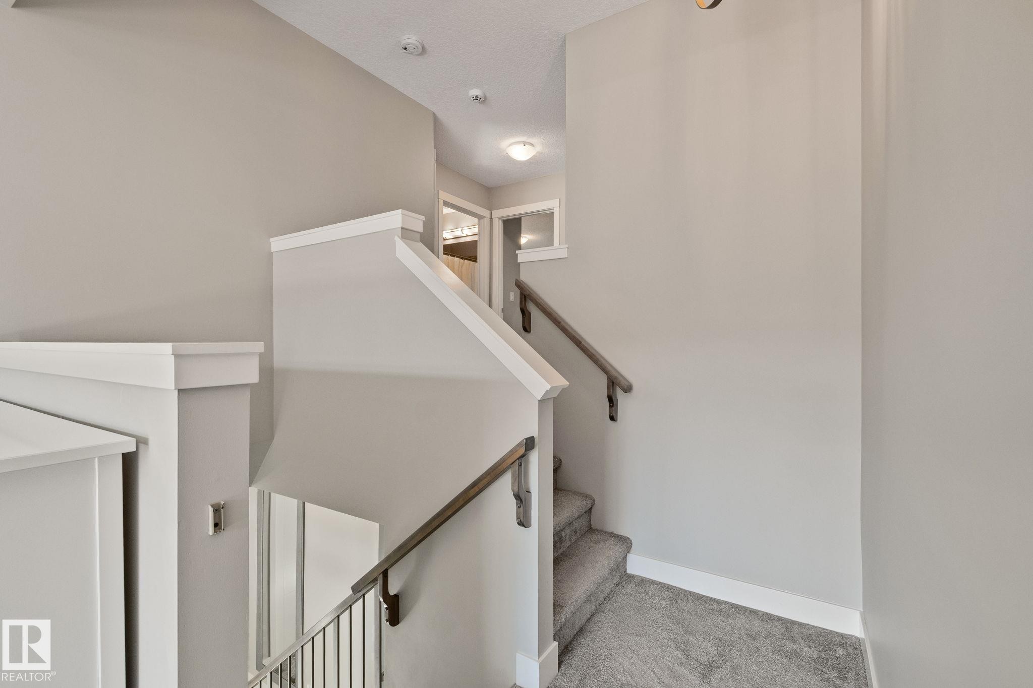 Carpeted staircase with wood handrails, painted risers, and white trim - 2096 Redtail Common Nw, Edmonton, AB
