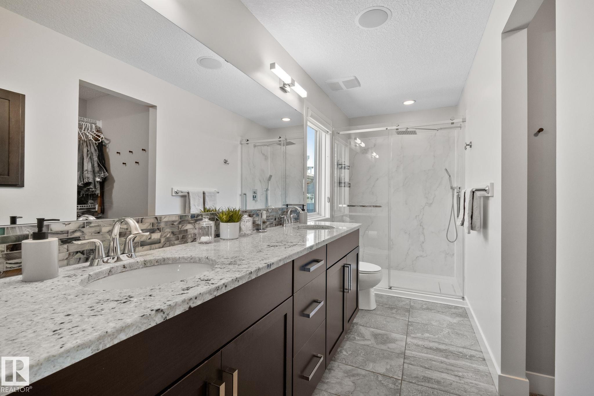 Dual vanity with stone countertop, dark wood-finish cabinetry, tile flooring, and a glass-enclosed shower with a tiled surround - 2096 Redtail Common Nw, Edmonton, AB
