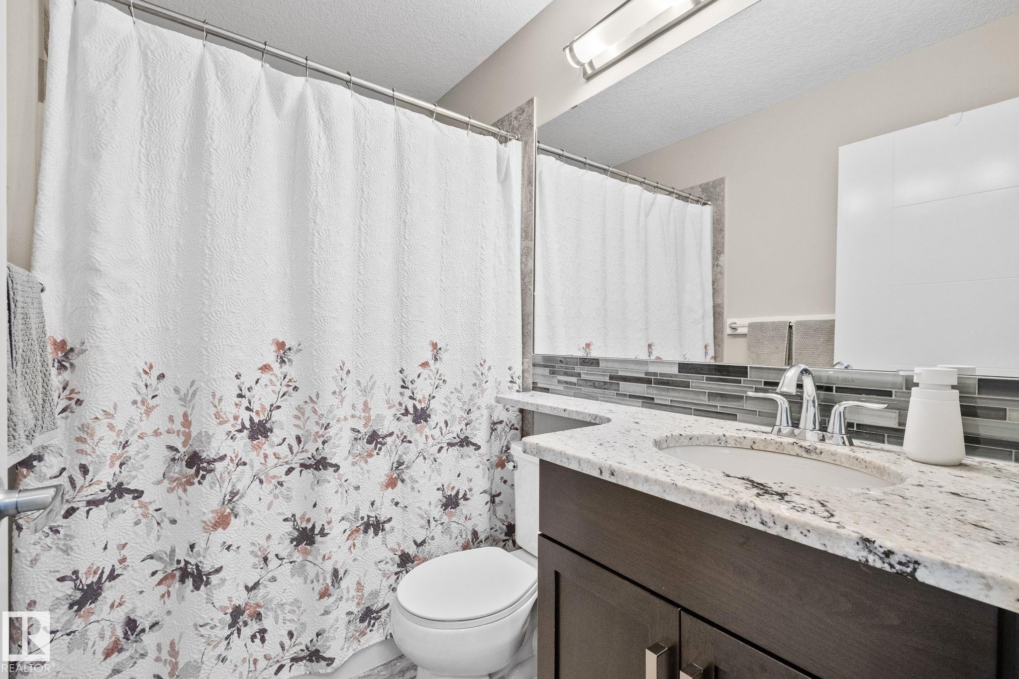 Vanity with an undermount sink, stone countertop, and mosaic tile backsplash - 2096 Redtail Common Nw, Edmonton, AB