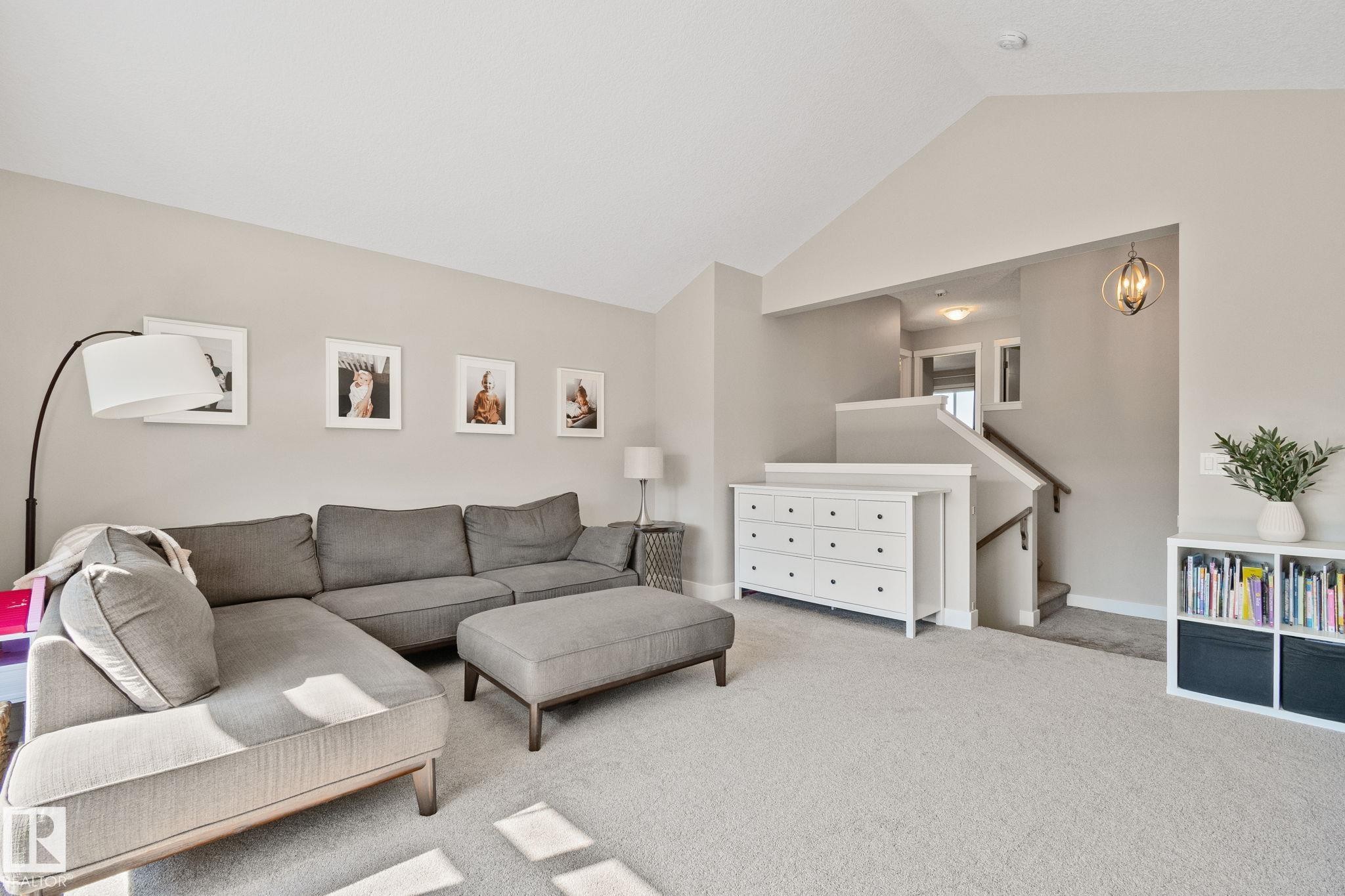 Vaulted ceiling over carpeted living area, featuring a staircase with wood handrails and a decorative overhead light fixture - 2096 Redtail Common Nw, Edmonton, AB
