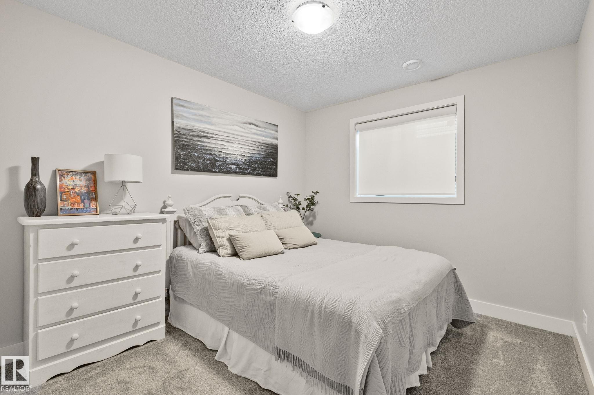 Bright secondary bedroom featuring neutral décor, carpet flooring, a double-hung window with cellular shades, and a white three-drawer dresser with integrated hardware - 2096 Redtail Common Nw, Edmonton, AB