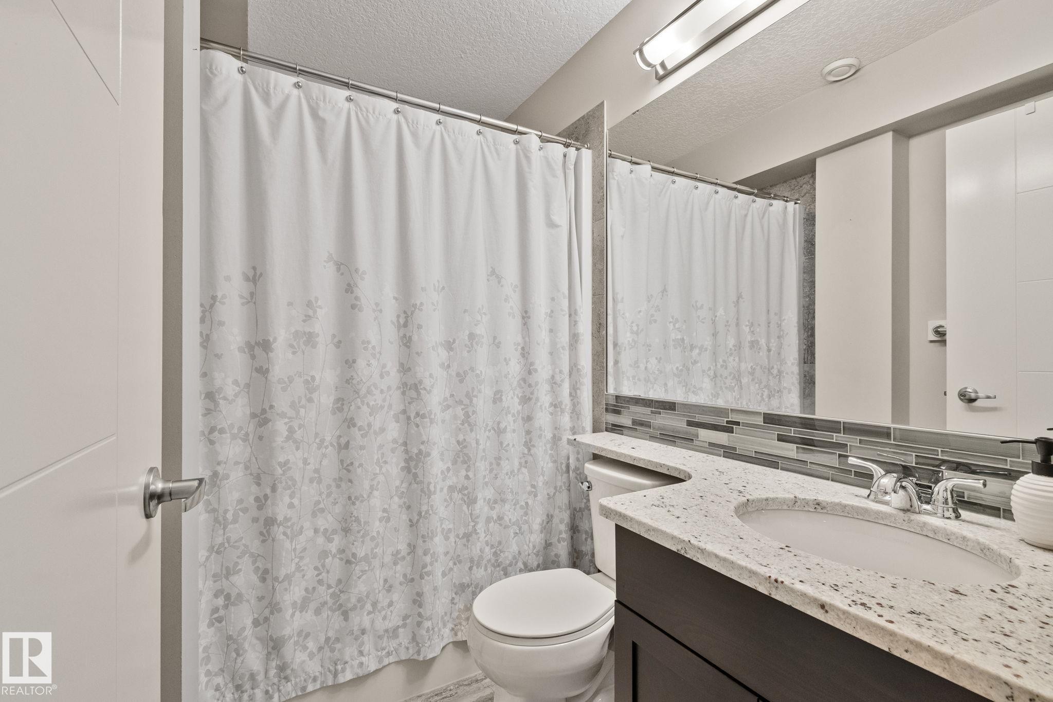 Bathroom featuring a vanity with an integrated sink, polished chrome faucet, and a stone-finish countertop - 2096 Redtail Common Nw, Edmonton, AB