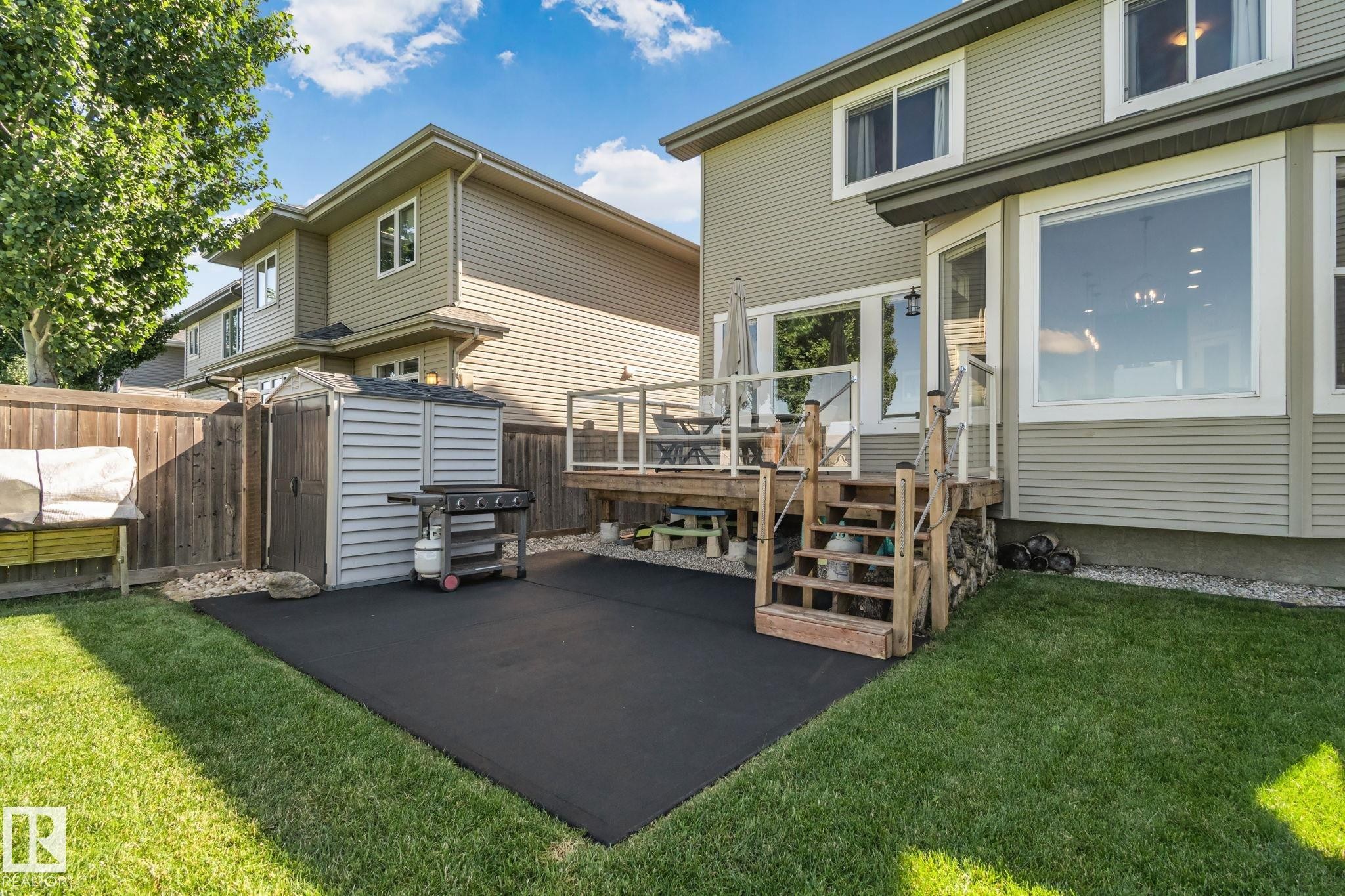 Expansive backyard featuring a wood deck with glass railing, a ground-level patio, a storage shed, and mature perimeter fencing - 2096 Redtail Common Nw, Edmonton, AB