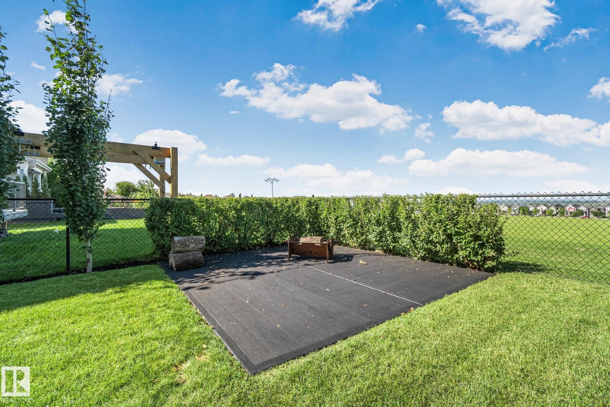 Expansive lawn, chain-link perimeter fencing, mature perimeter hedges, and a dedicated outdoor patio area - 2096 Redtail Common Nw, Edmonton, AB
