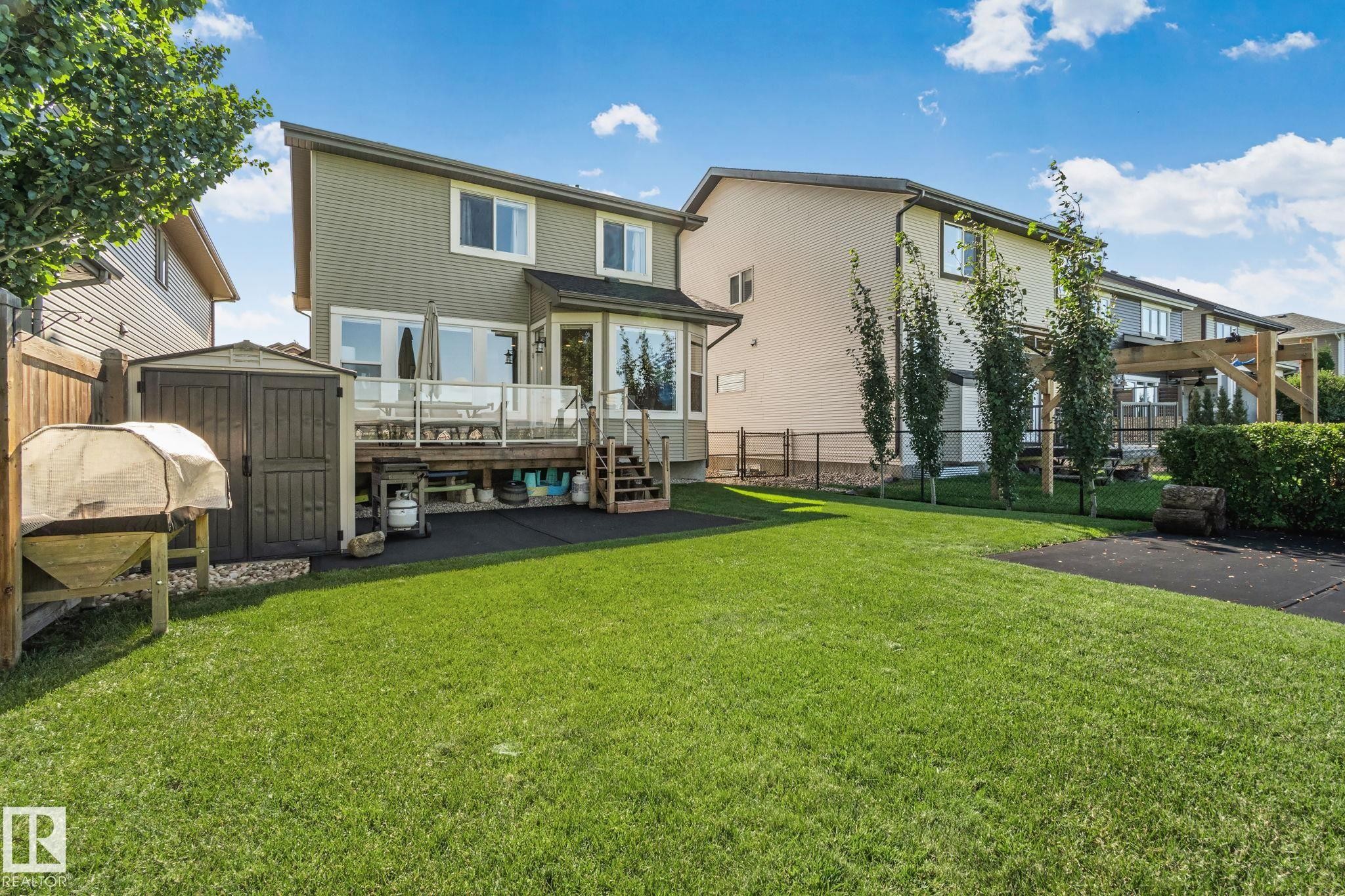 Expansive backyard featuring a lush lawn, a multi-level deck with glass railings, a storage shed, and mature trees - 2096 Redtail Common Nw, Edmonton, AB