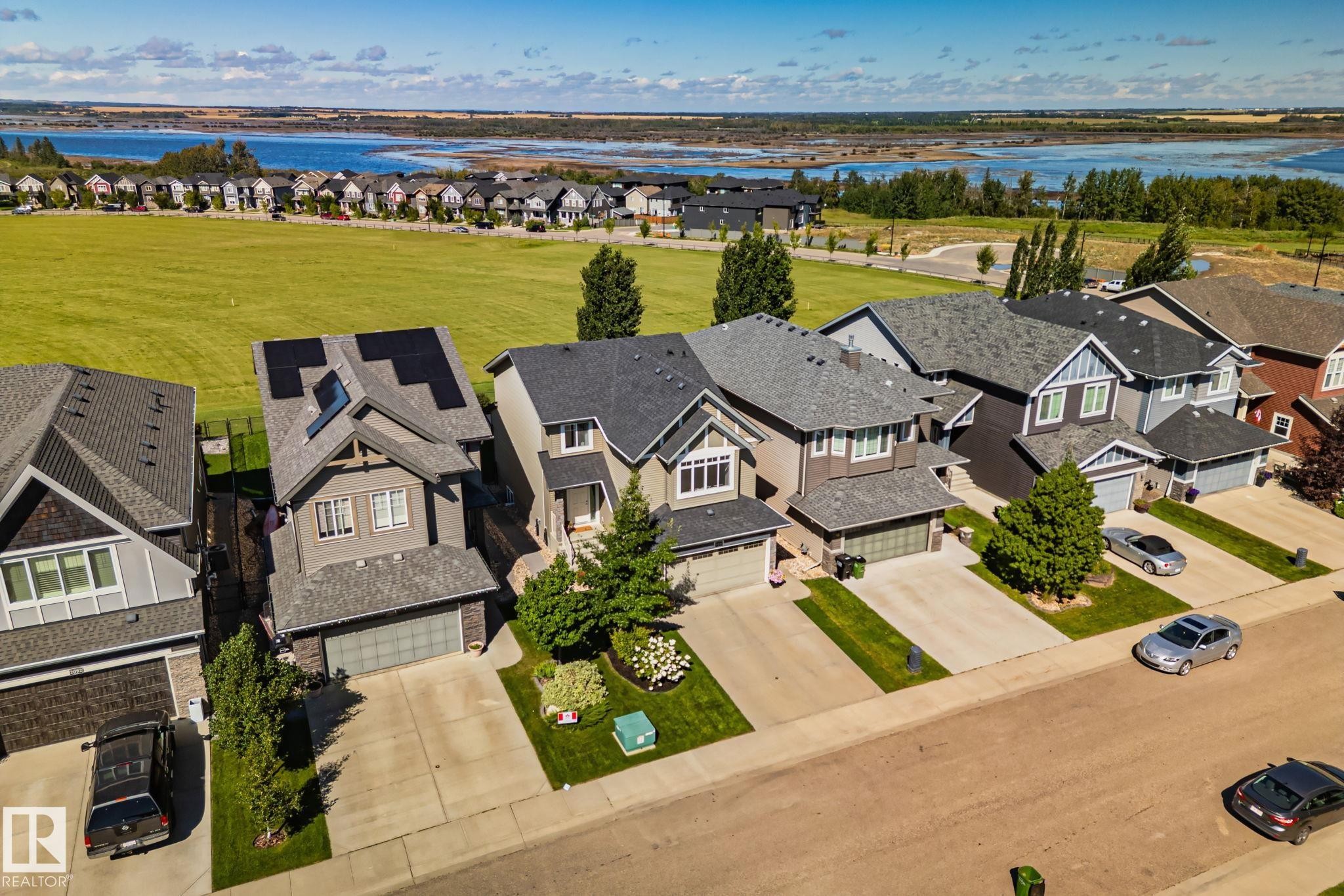 Residential street with neatly maintained lawns, mature trees, and an expansive green space - 2096 Redtail Common Nw, Edmonton, AB