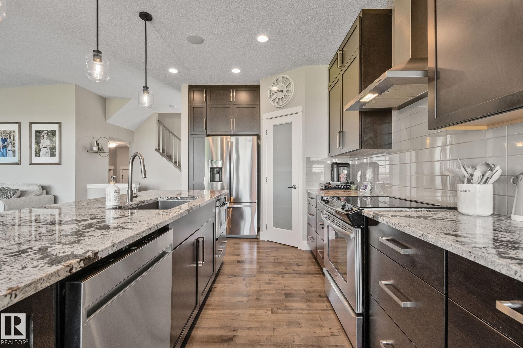 Expansive kitchen island with stone countertops, stainless steel appliances, dark wood cabinetry, and wood-finish flooring - 2096 Redtail Common Nw, Edmonton, AB