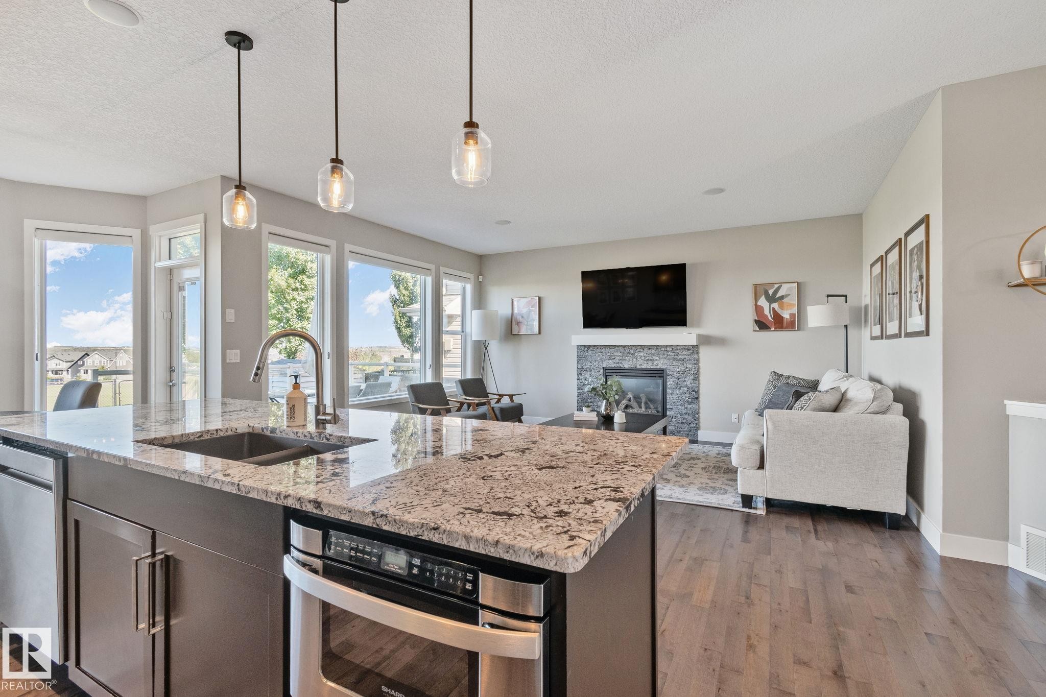 Spacious kitchen island with granite countertops, stainless steel appliances, and pendant lighting - 2096 Redtail Common Nw, Edmonton, AB