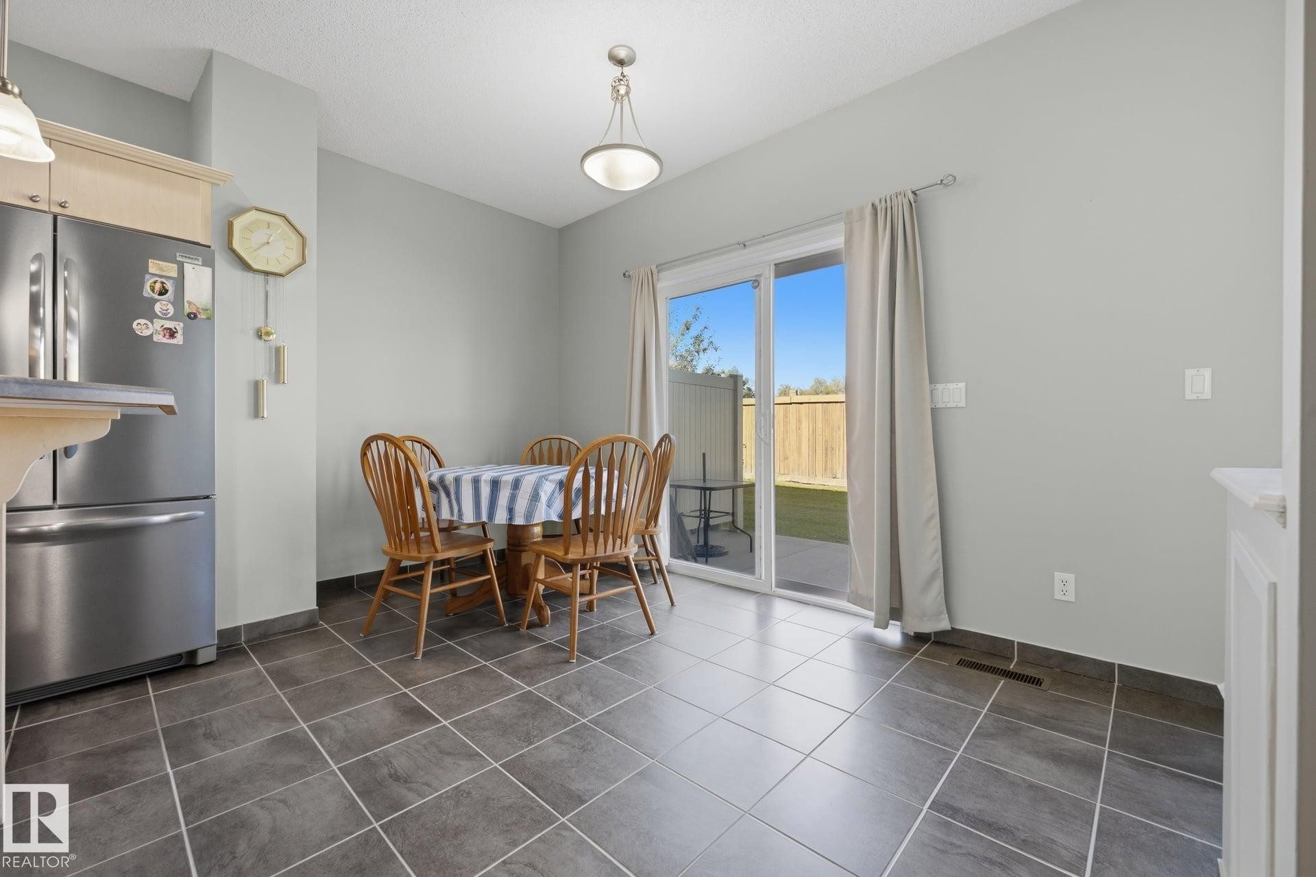 Ceramic tile flooring, sliding glass door, and a built-in kitchen peninsula with a stainless steel refrigerator - #102 13825 155 Av Nw, Edmonton, AB
