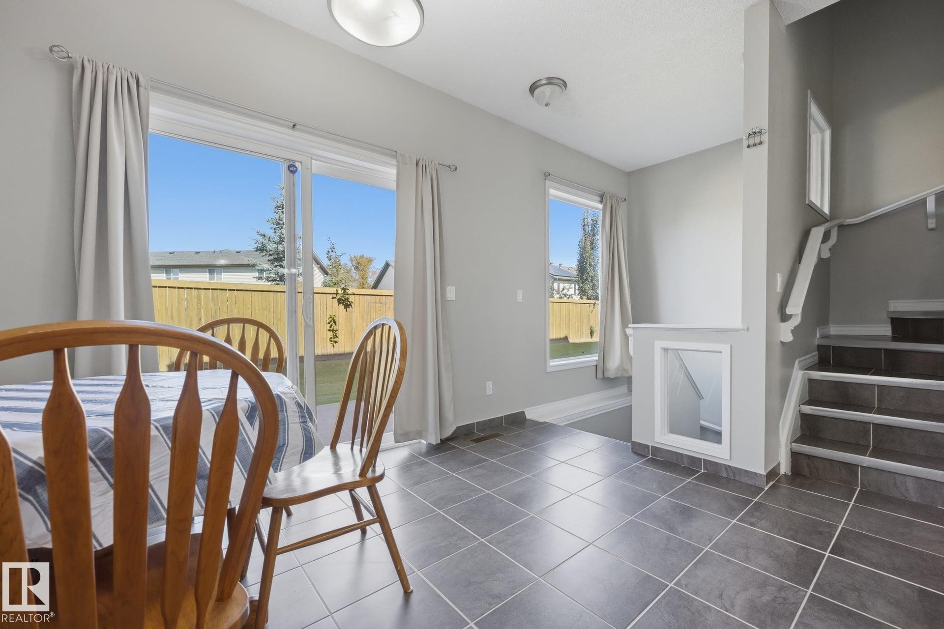 Tile flooring, sliding glass door, fixed window, fenced backyard, and staircase with railing - #102 13825 155 Av Nw, Edmonton, AB