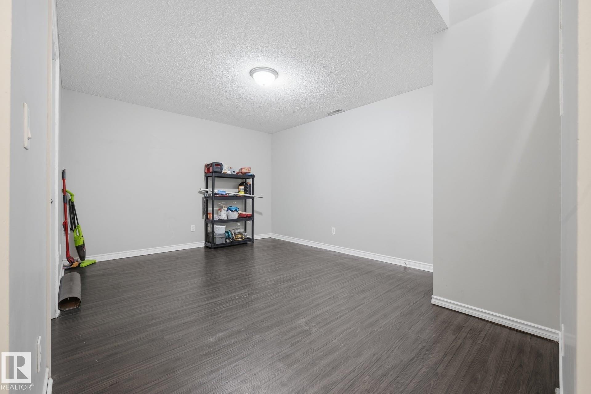 Spacious room featuring wood-finish flooring, light grey walls, and a recessed ceiling light fixture - #102 13825 155 Av Nw, Edmonton, AB