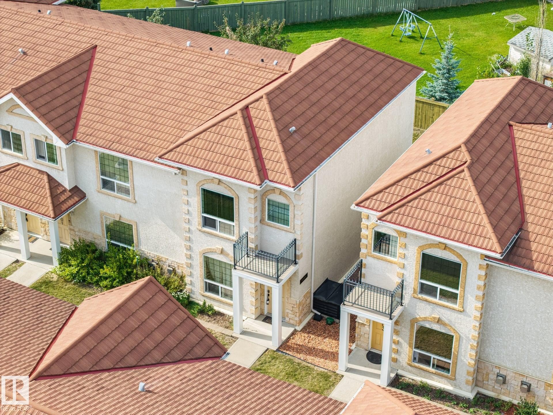 Stucco exterior with stone accents, arched window casings, terracotta-toned tile roofing, and upper-level balconies with wrought iron railings - #102 13825 155 Av Nw, Edmonton, AB