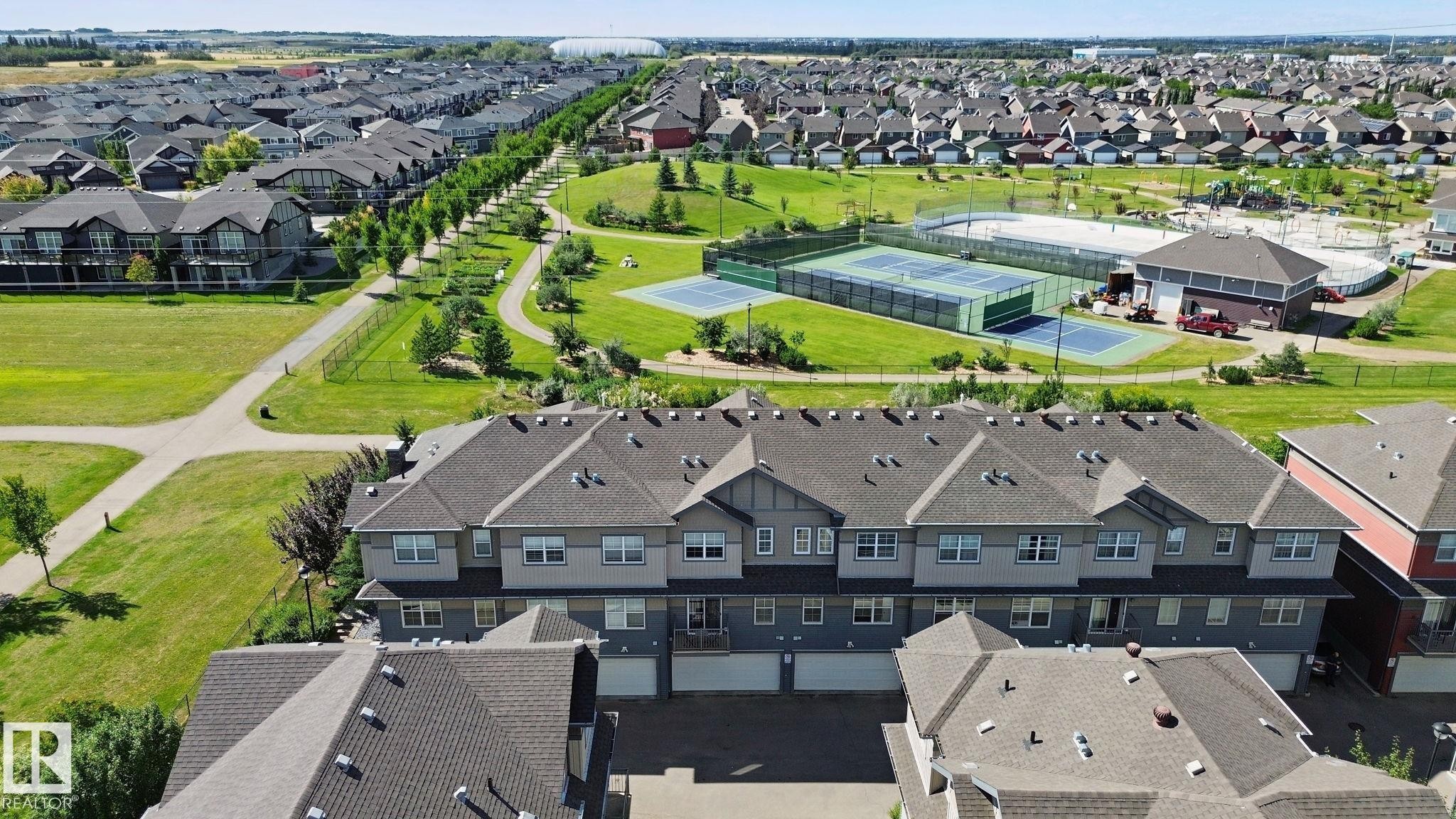 Multi-unit residential structures with attached garages, surrounded by extensive green spaces, paved pathways, and recreational courts - #58 4029 Orchards Dr Sw, Edmonton, AB