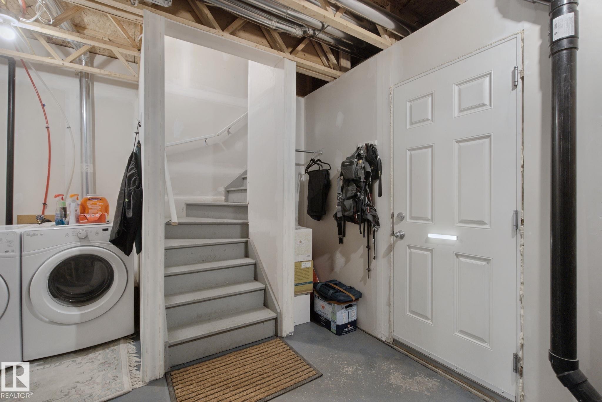 Laundry area featuring a front-loading washing machine, adjacent to a staircase with a handrail - #58 4029 Orchards Dr Sw, Edmonton, AB