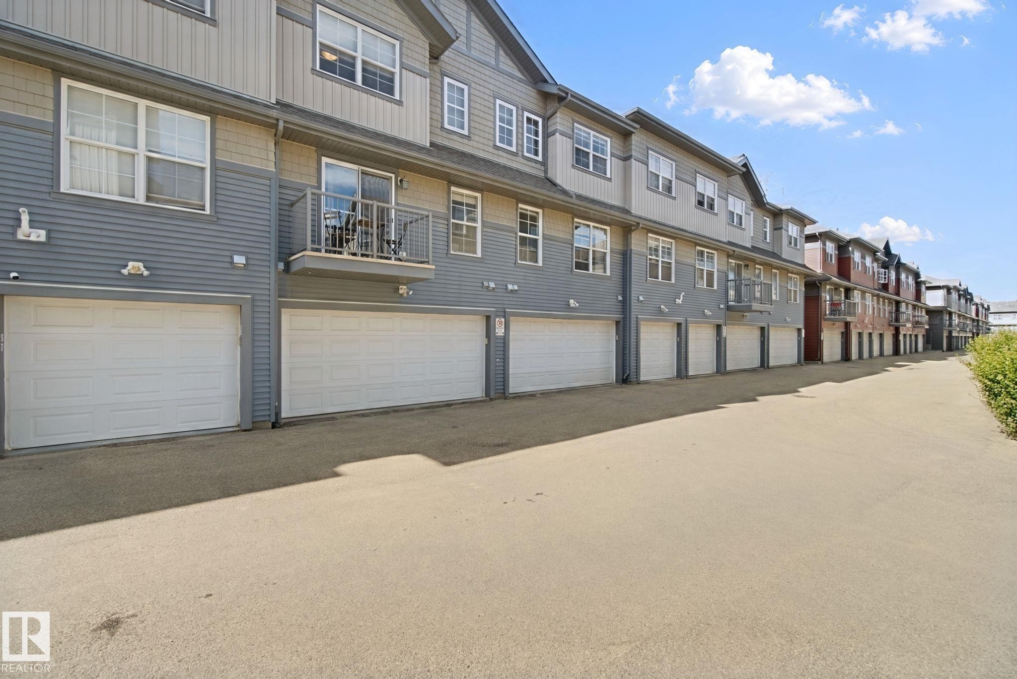 Multi-level townhouse exterior with dual-toned siding, attached garages, and private balconies with metal railings - #58 4029 Orchards Dr Sw, Edmonton, AB