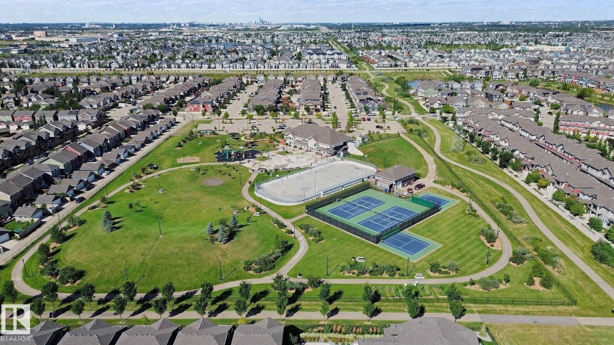 Expansive green space featuring multiple tennis courts, a recreational rink, a playground, and paved walking paths - #58 4029 Orchards Dr Sw, Edmonton, AB