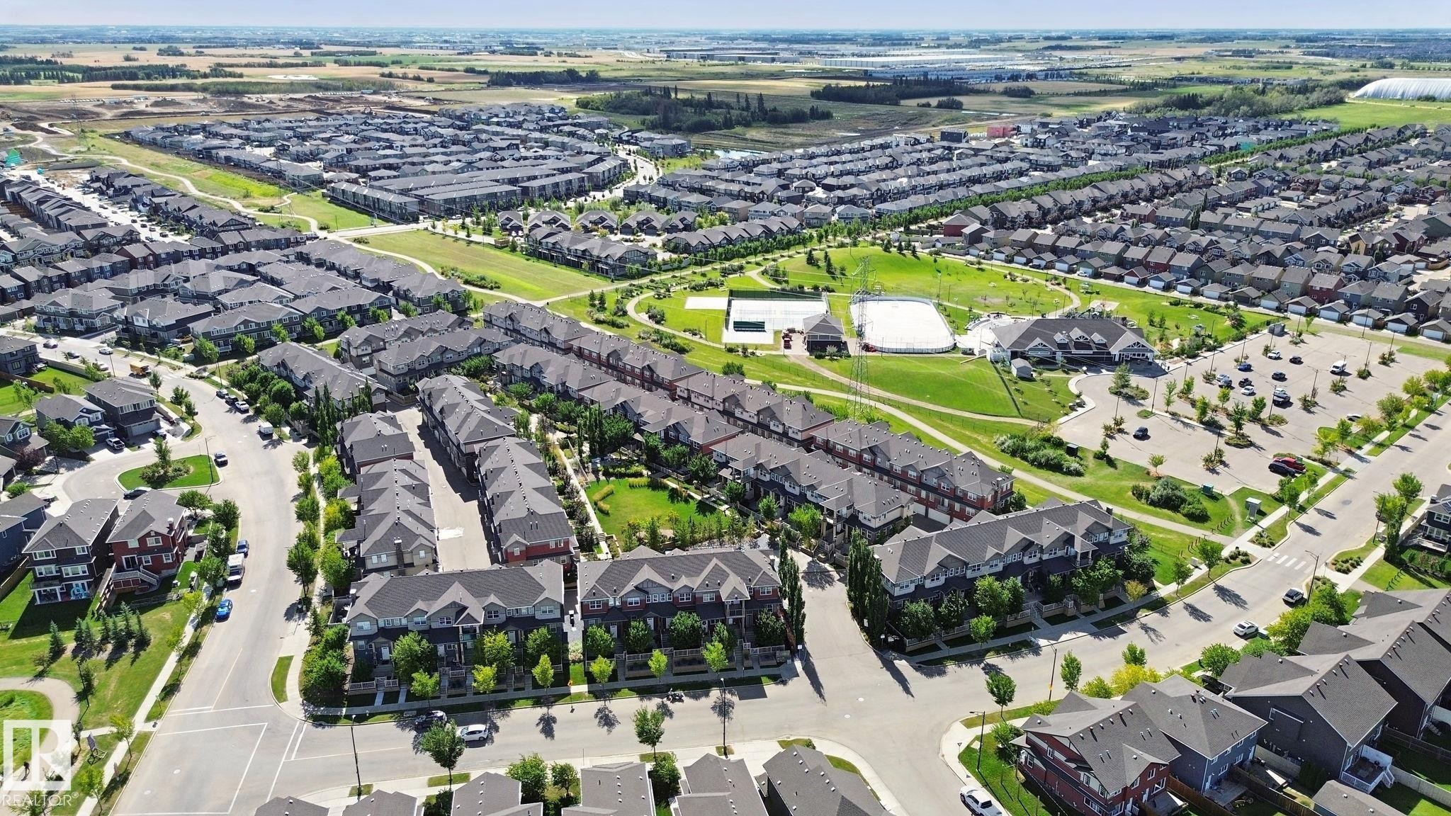 Expansive community featuring residential buildings, a large asphalt parking area, and green spaces with walking paths - #58 4029 Orchards Dr Sw, Edmonton, AB