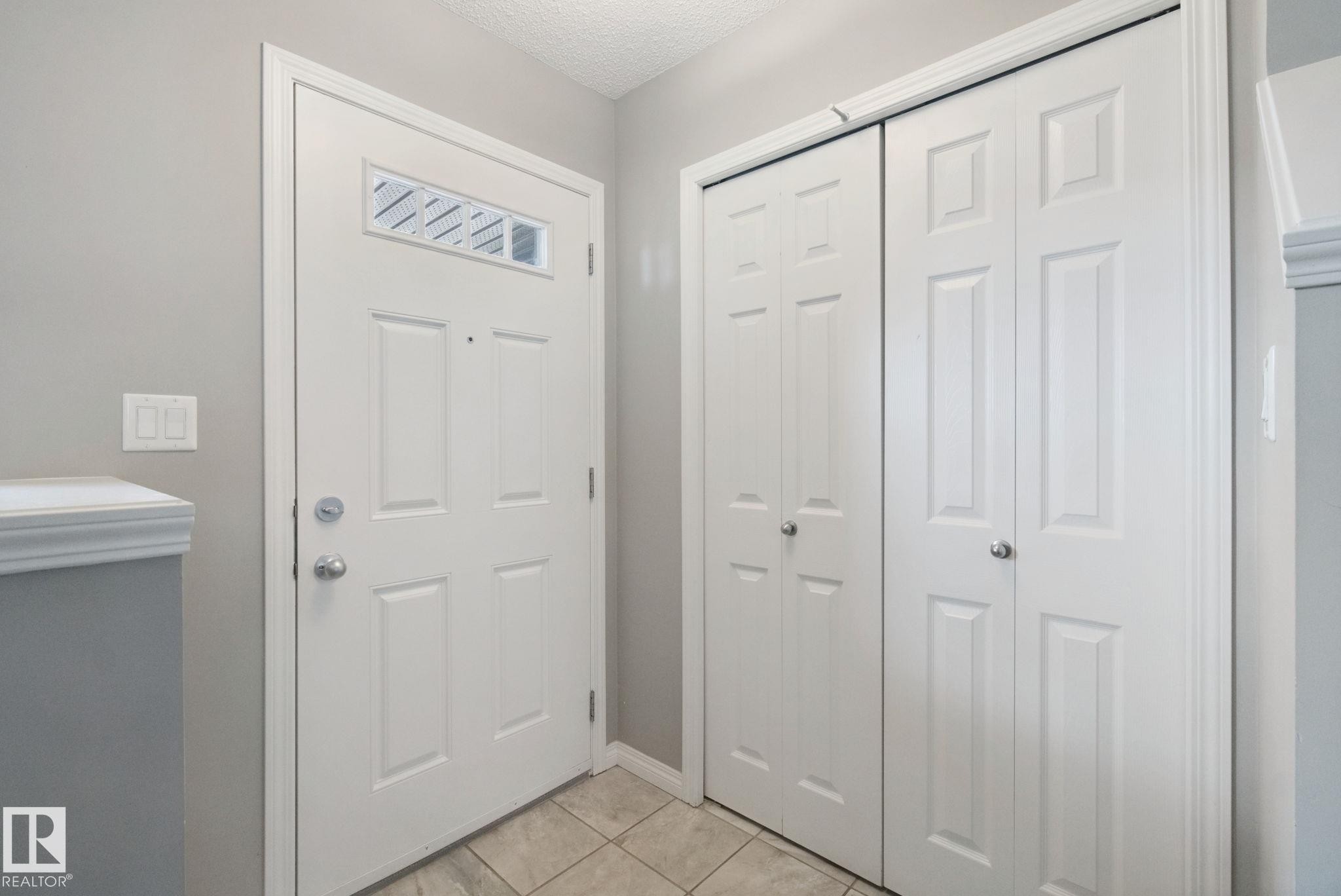 Entryway with tile flooring, a white paneled door featuring an upper window, and bi-fold closet doors - #58 4029 Orchards Dr Sw, Edmonton, AB