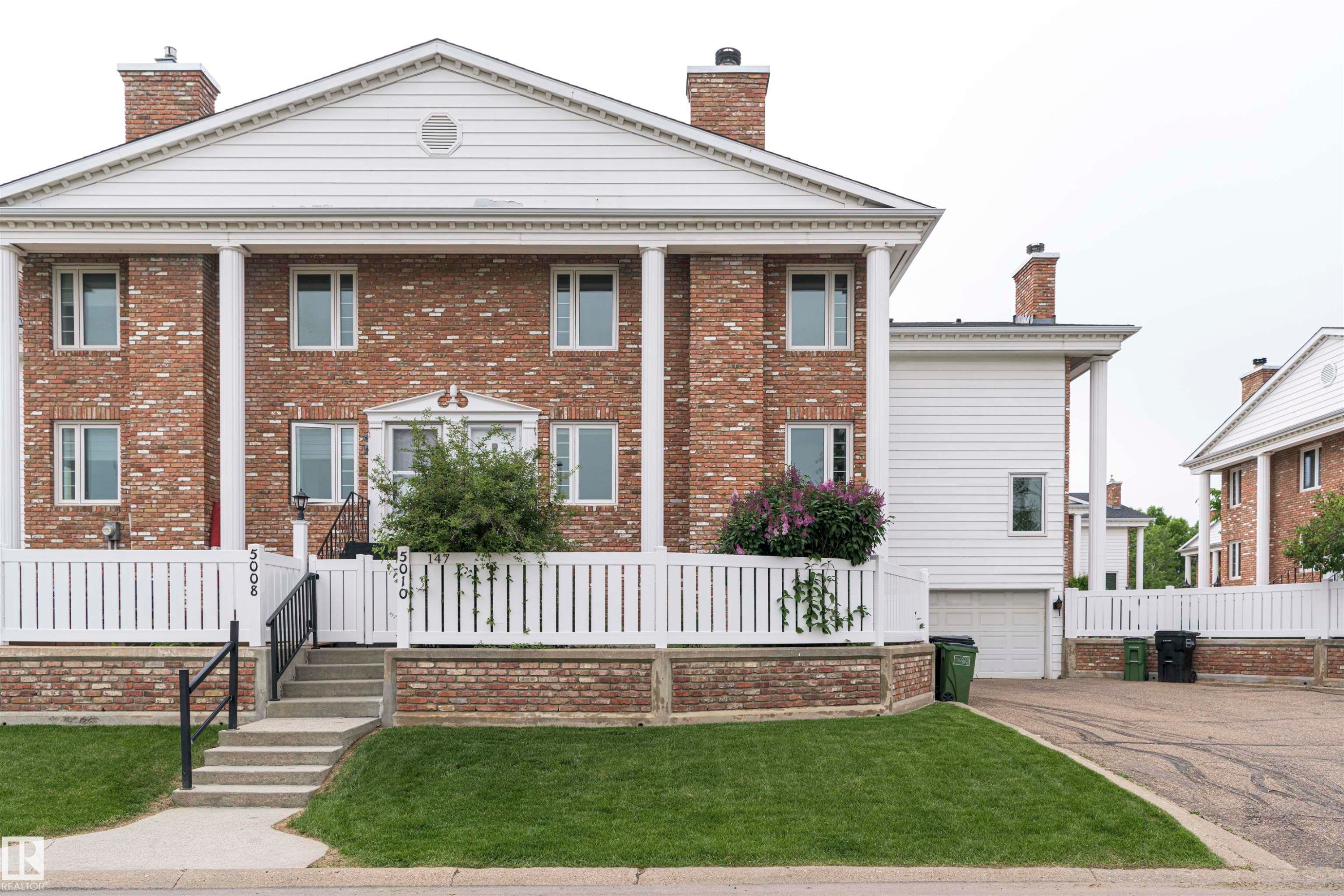 Brick facade residence featuring a white portico supported by four columns, a prominent pediment, and a white picket fence enclosing the front yard - 5010 147 Street Nw, Edmonton, AB