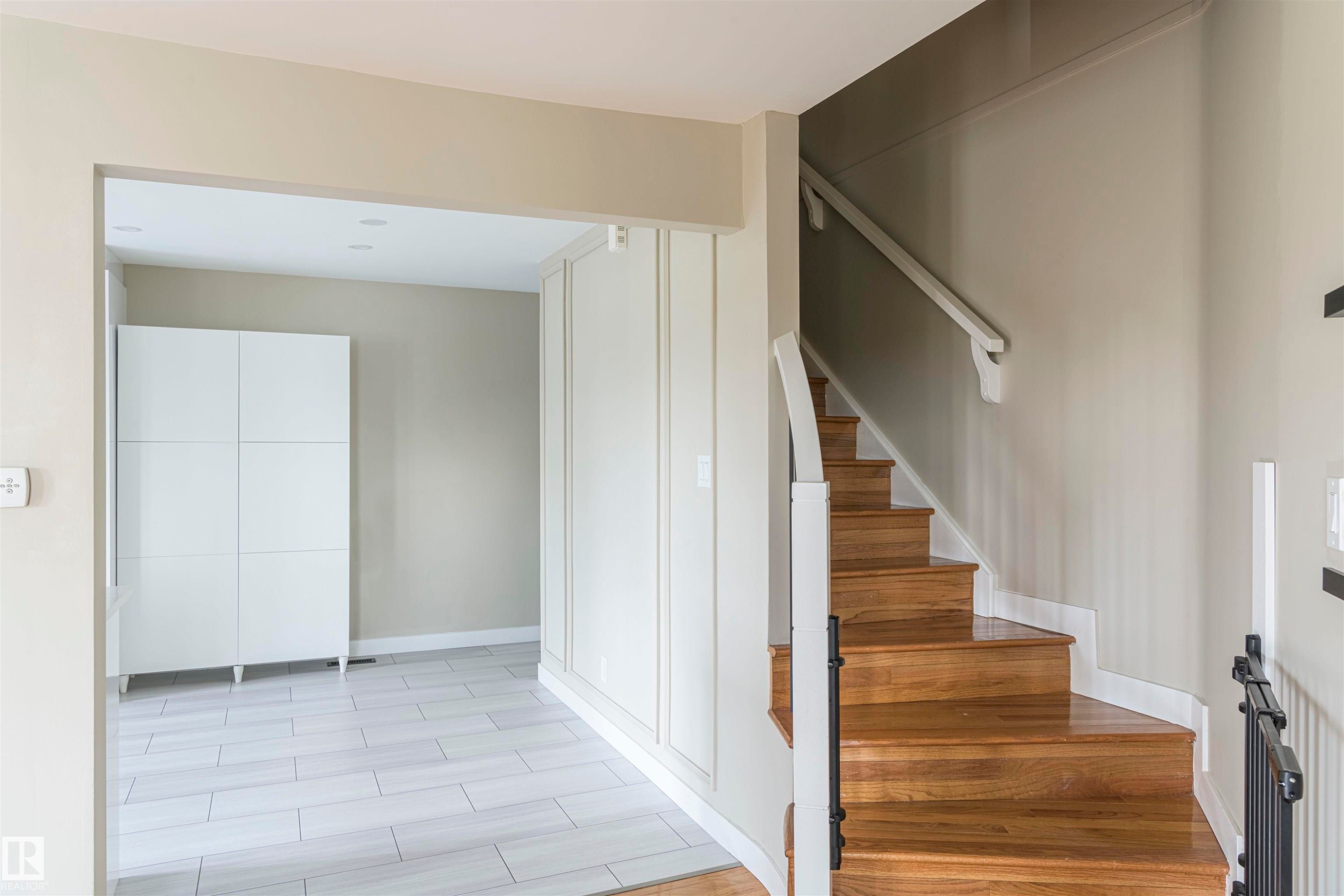 Entryway featuring a wood staircase with white risers and a white handrail, complemented by a black metal baluster - 5010 147 Street Nw, Edmonton, AB