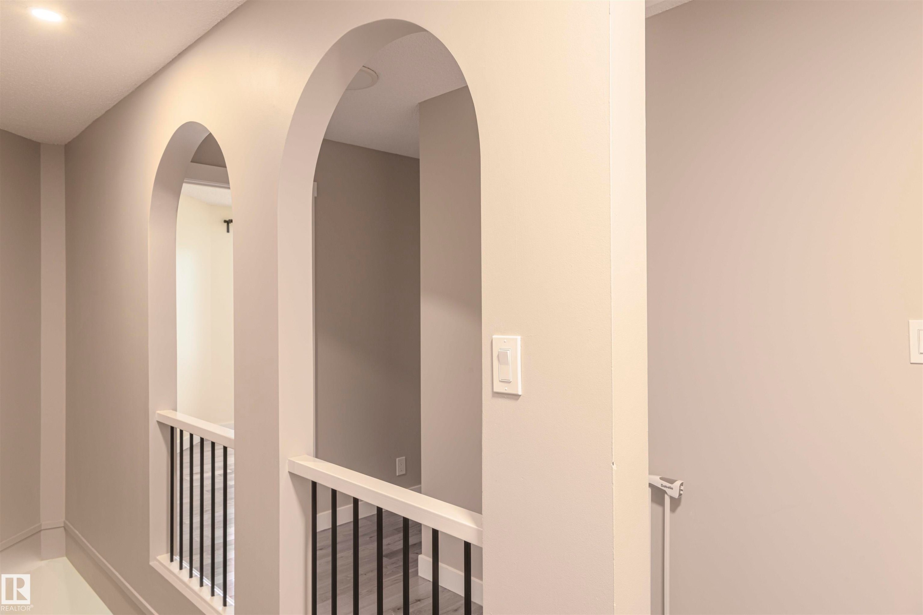 Hallway featuring arched doorways, recessed lighting, white balusters with black spindles, and light-toned wall paint - 5010 147 Street Nw, Edmonton, AB