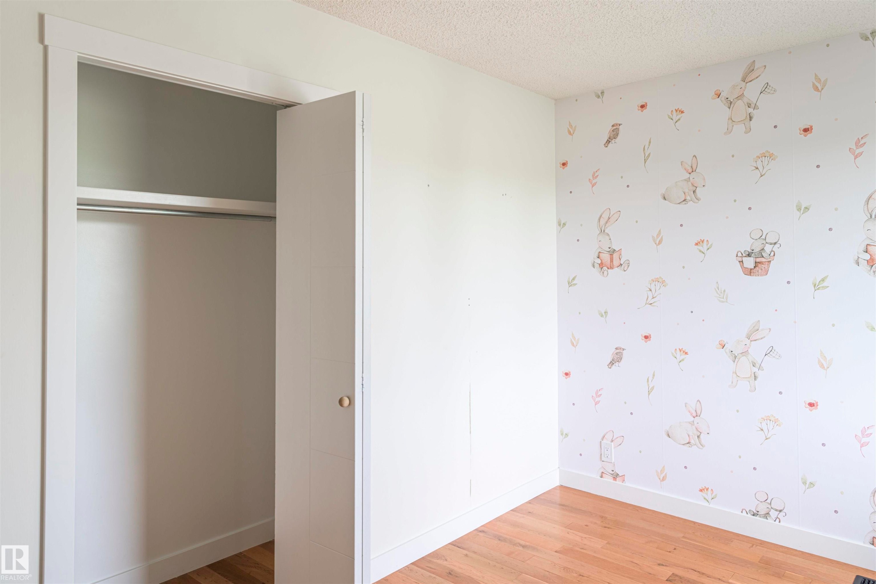 Bedroom featuring wood-finish flooring, a bi-fold closet door, and a decorative accent wall - 5010 147 Street Nw, Edmonton, AB