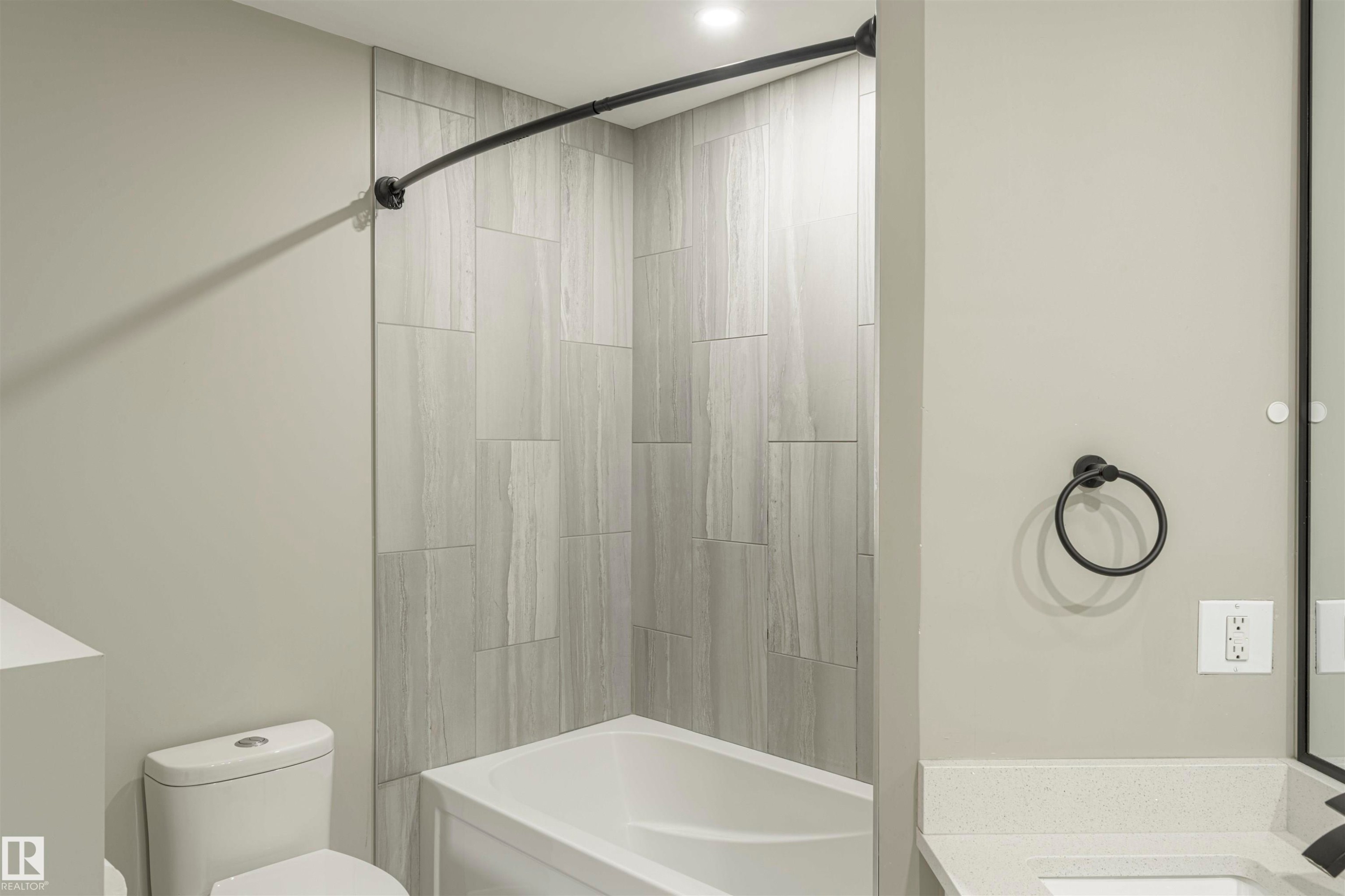 Bathtub and shower combination featuring large format grey tile surround and a curved matte black shower rod - 5010 147 Street Nw, Edmonton, AB