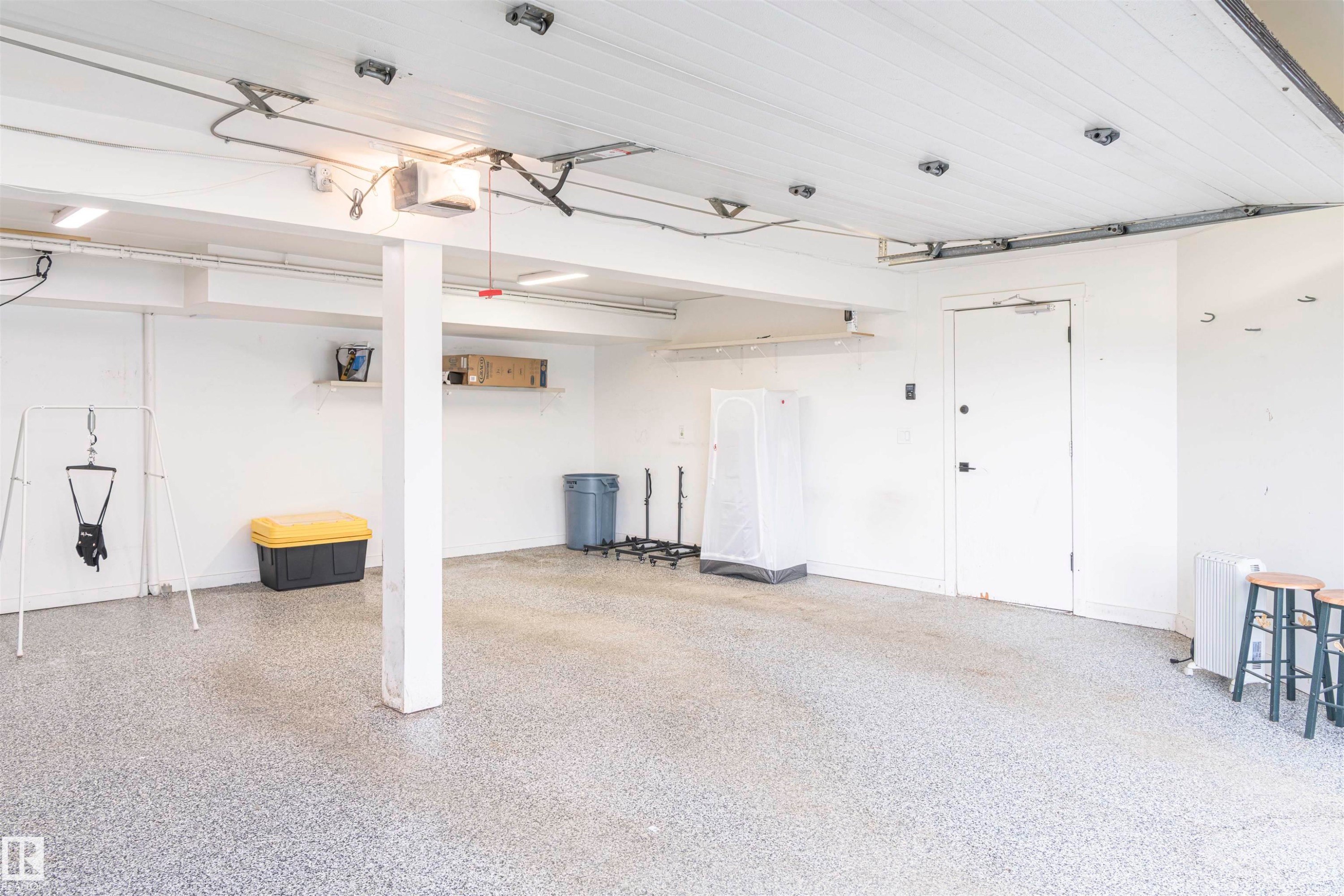 Spacious garage featuring a durable epoxy speckled floor, white paneled ceiling, and ample wall shelving - 5010 147 Street Nw, Edmonton, AB