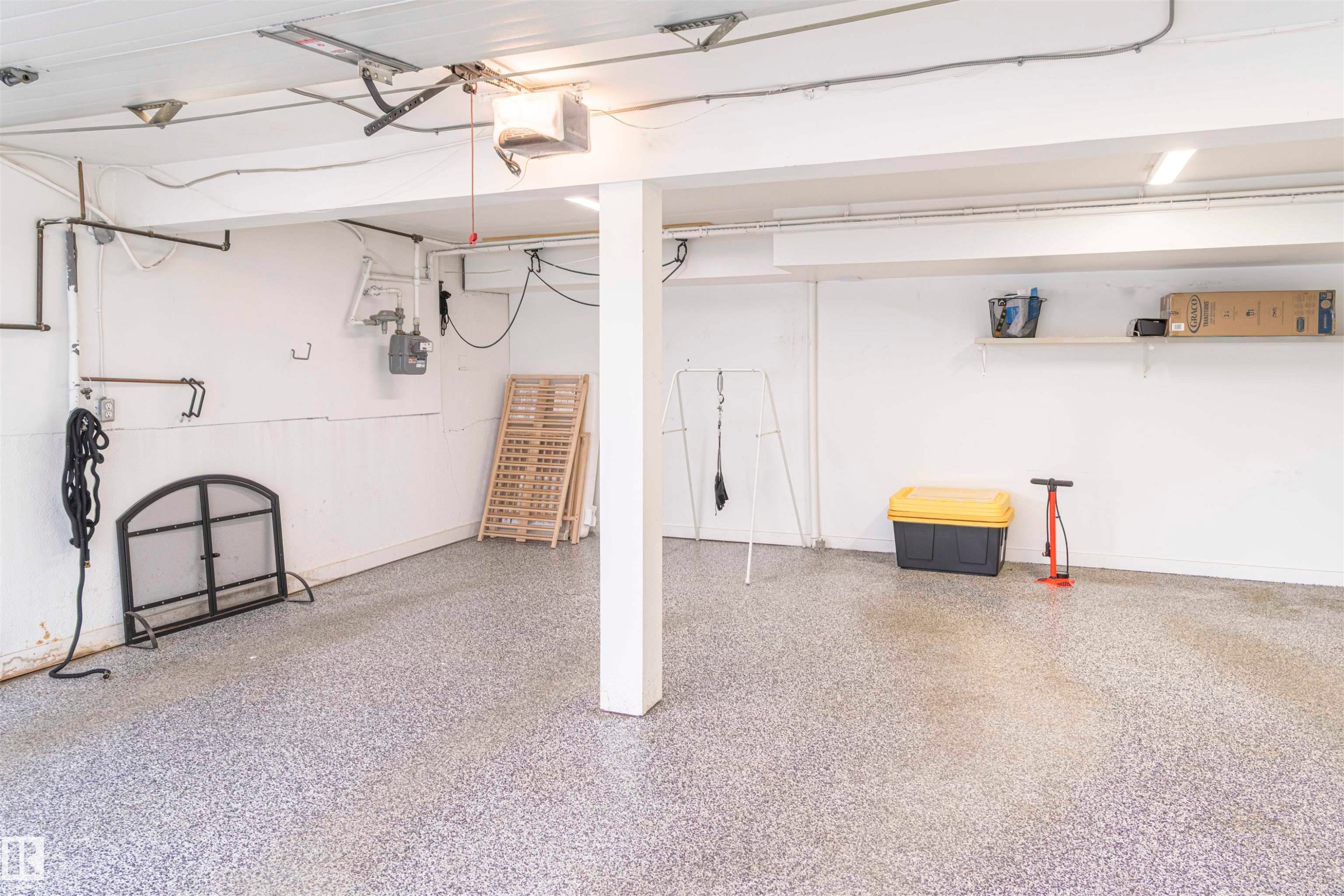 Spacious garage featuring a durable speckled epoxy floor, overhead lighting, an exposed beam ceiling, and a built-in wall shelf - 5010 147 Street Nw, Edmonton, AB