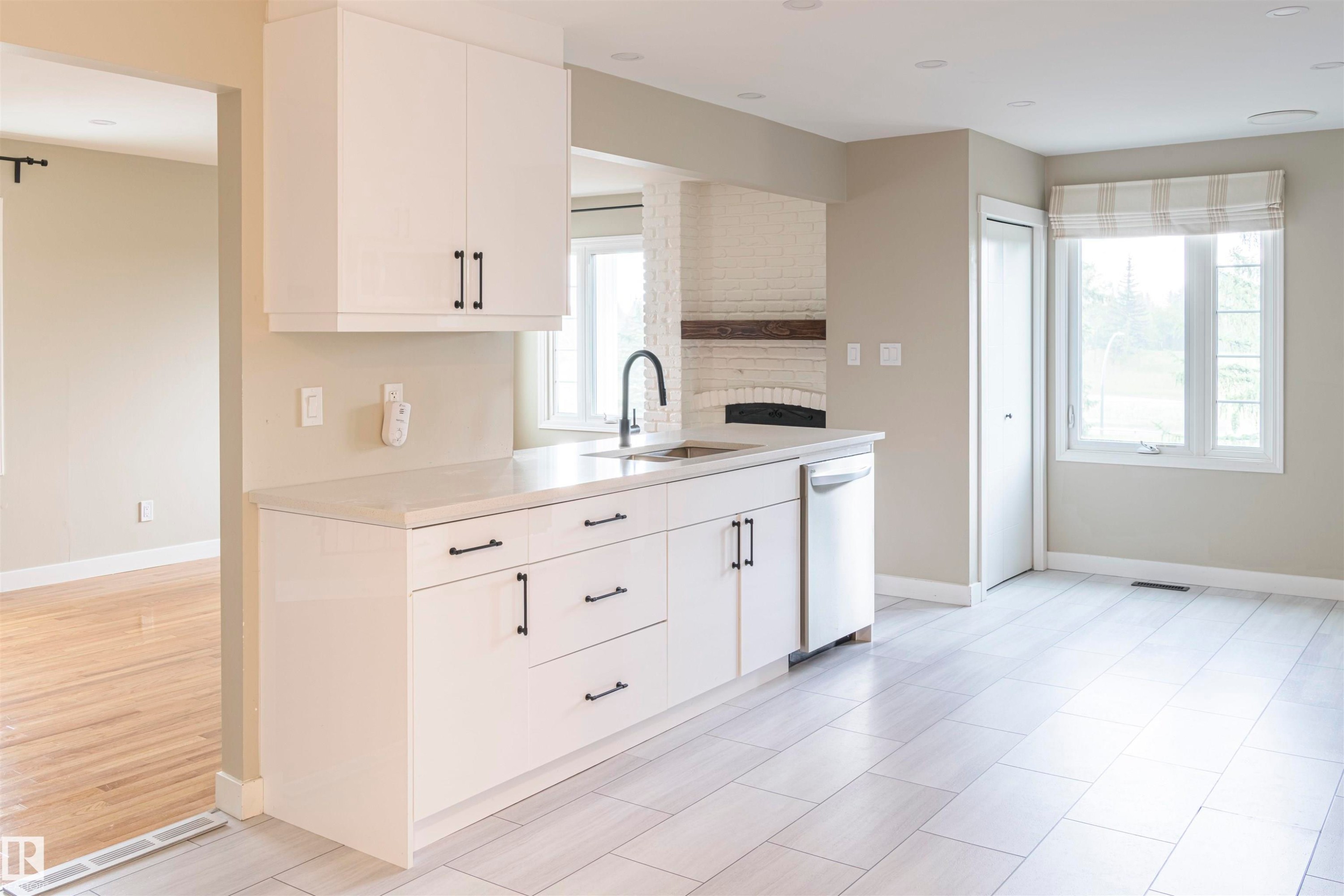 Modern kitchen featuring white cabinetry with black hardware, a stainless steel dishwasher, and a black gooseneck faucet - 5010 147 Street Nw, Edmonton, AB