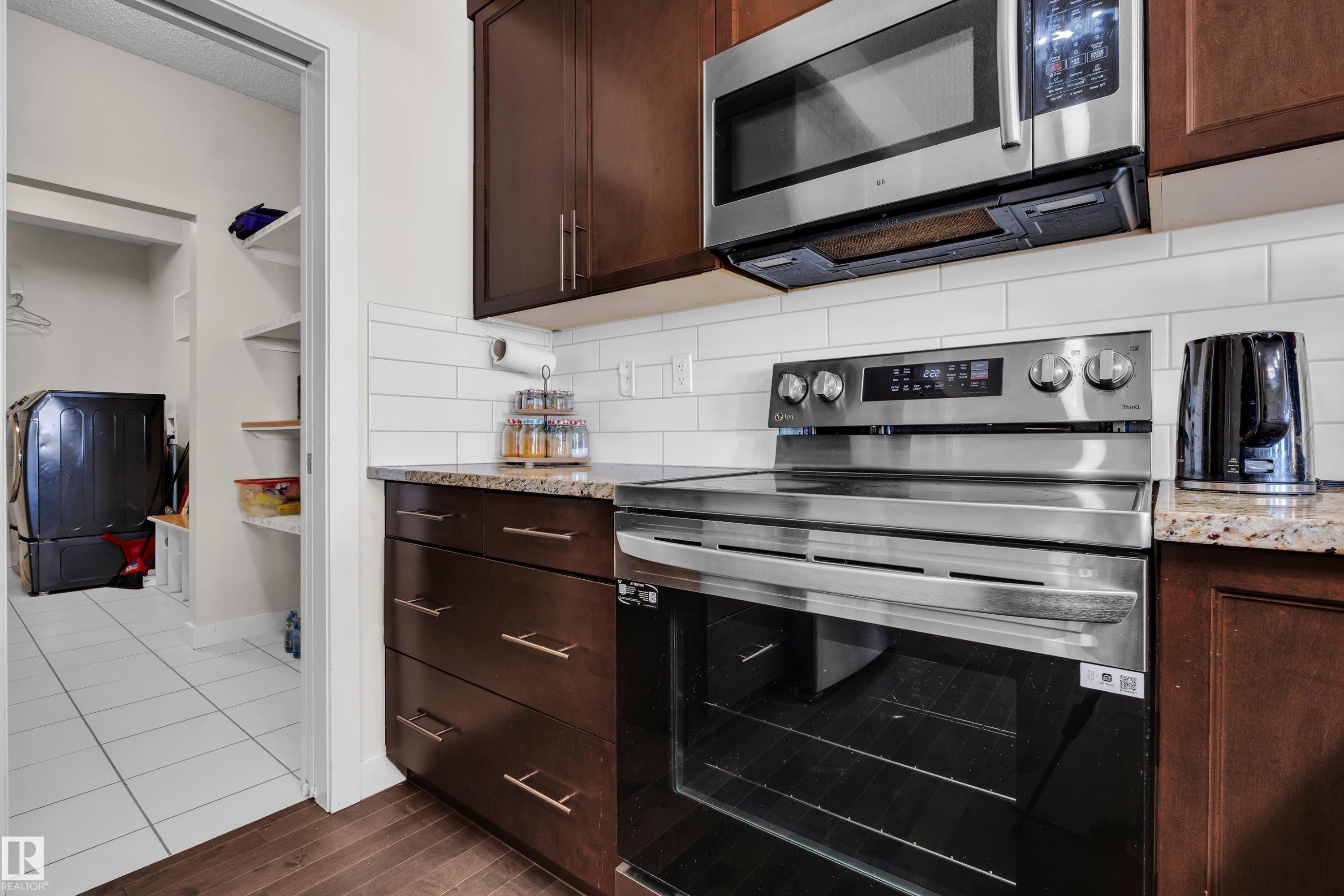Kitchen area featuring rich wood-finish cabinetry with stainless steel appliances, granite-style countertops, and a subway tile backsplash - 3071 Carpenter Landing Sw, Edmonton, AB